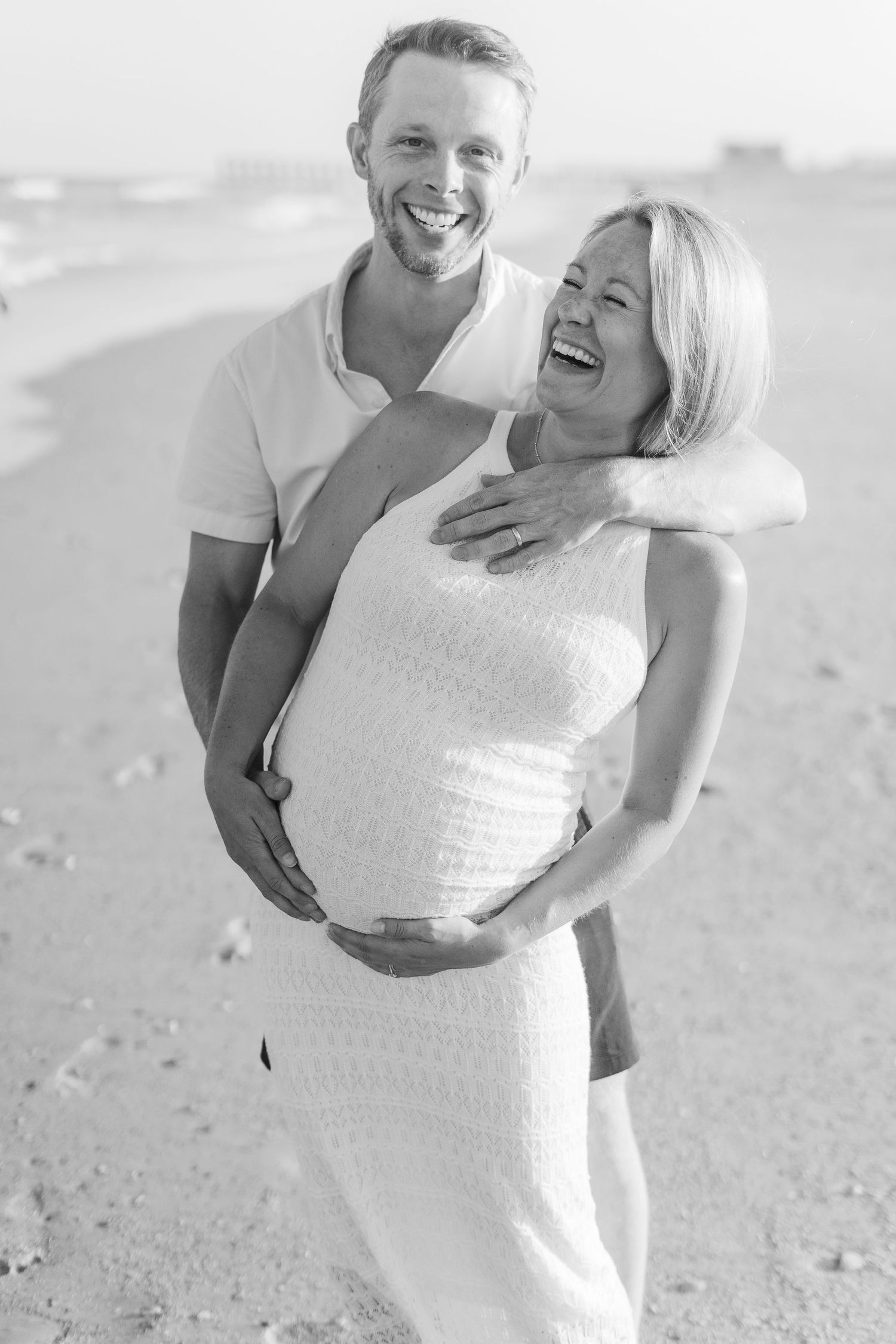 Happy expectant couple laughing together during beach maternity session.