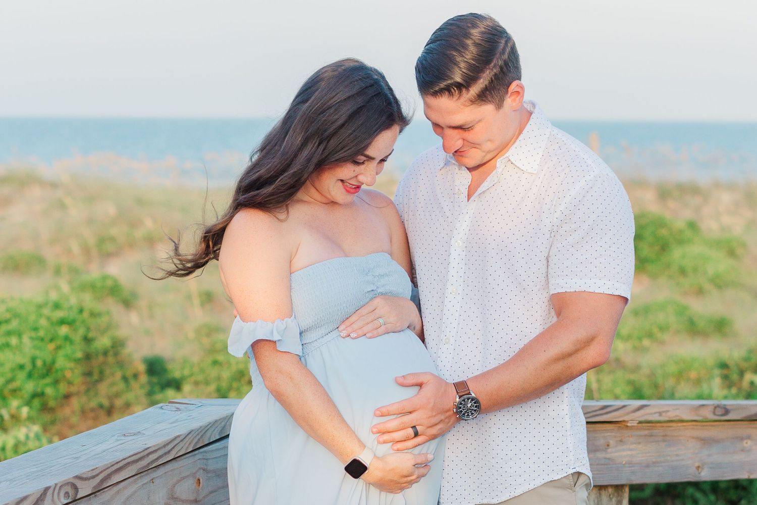 A tender maternity moment captured outdoors with the ocean in the background.