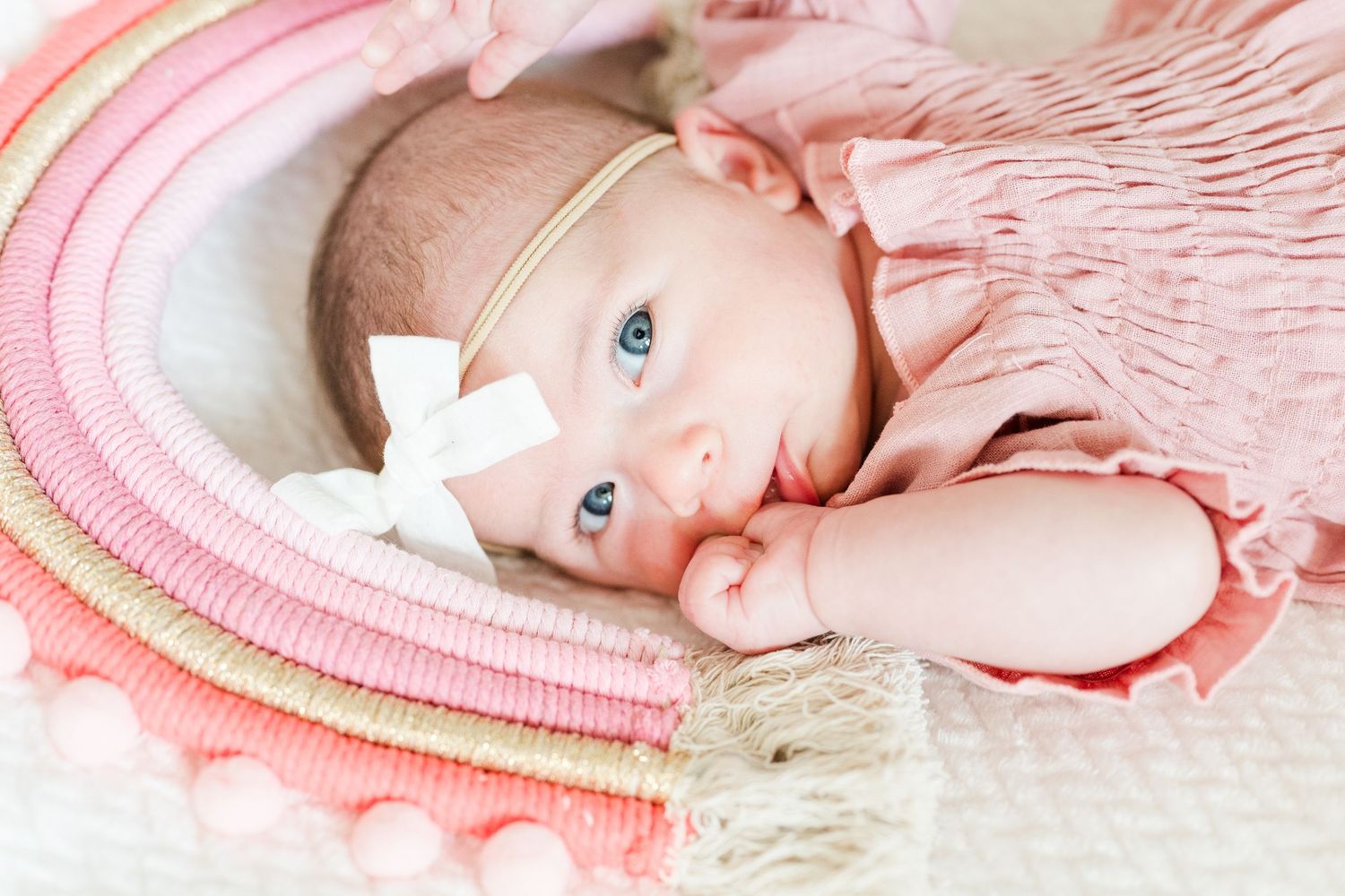 Baby in pink outfit laying on soft textured blankets with knit details and white bow headband.