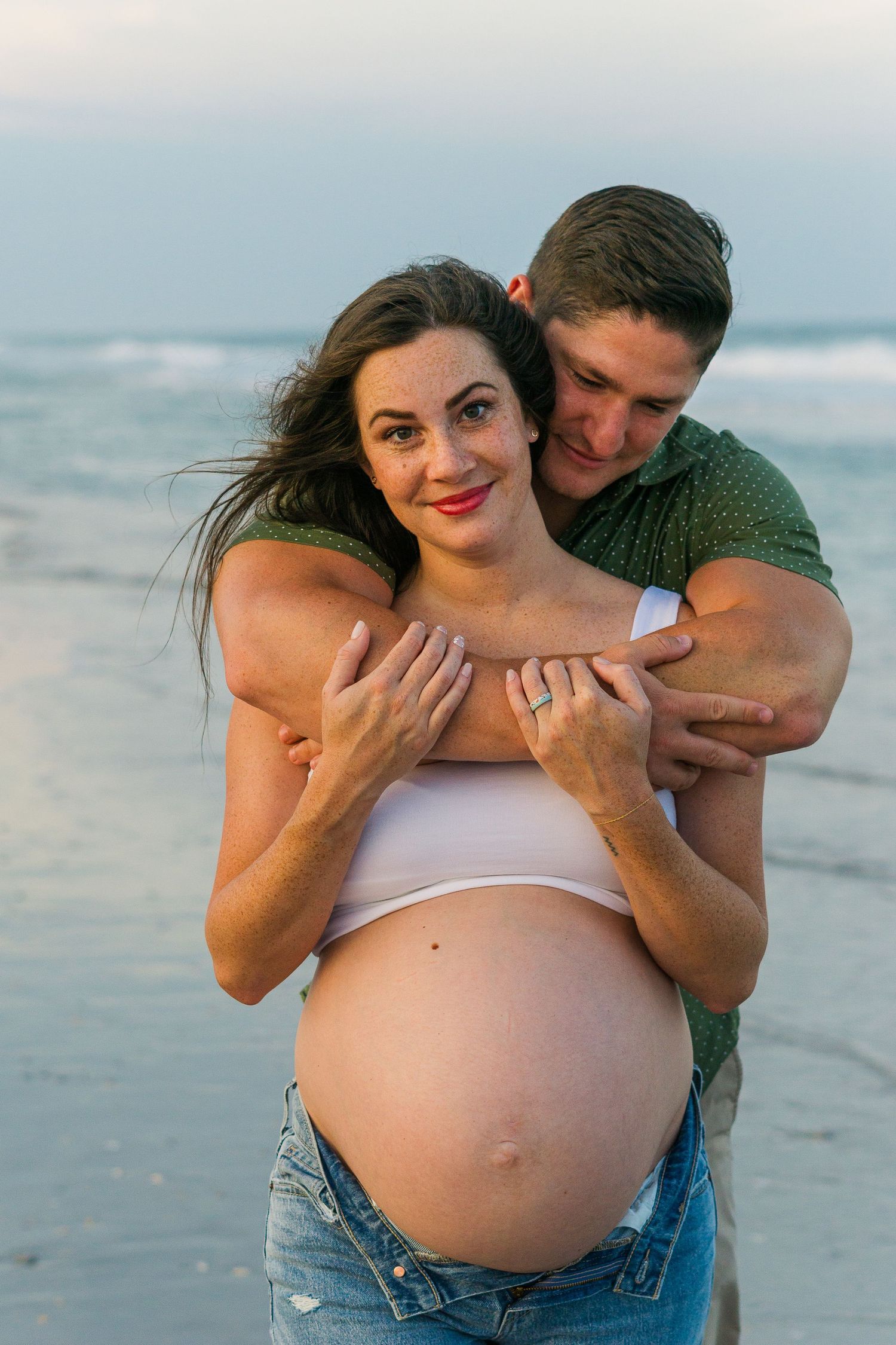 Intimate beach maternity portrait with couple embracing against ocean backdrop.
