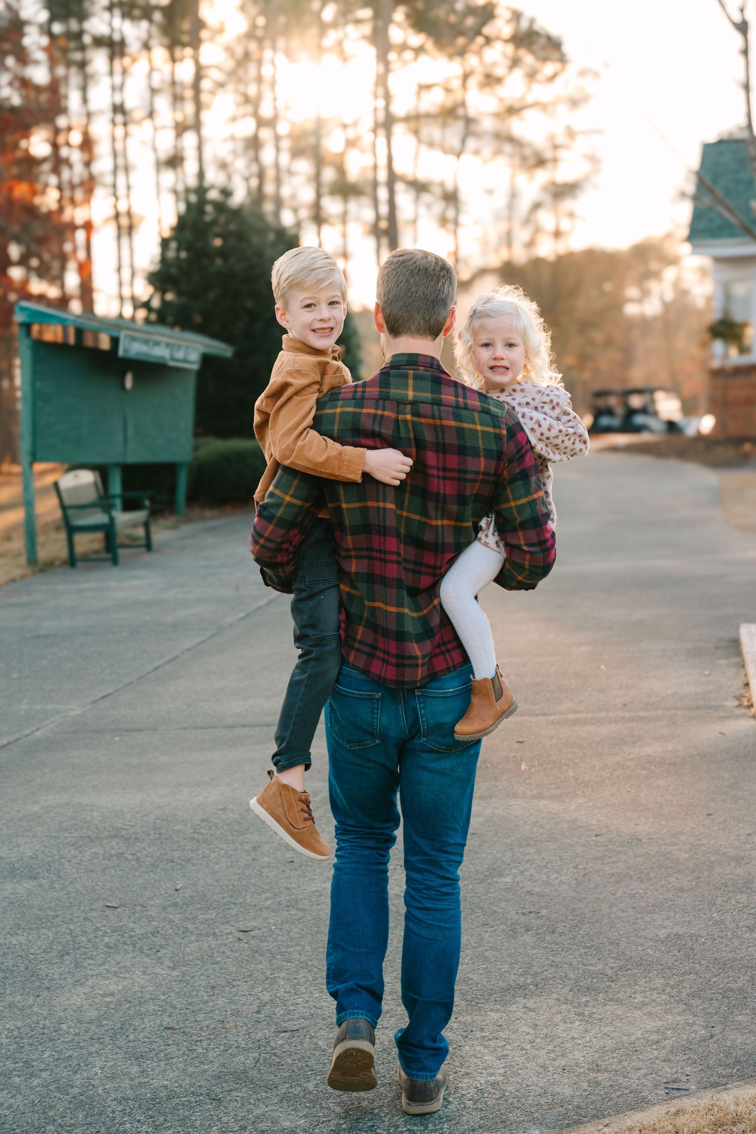 Person carrying two children while walking on path during sunset.