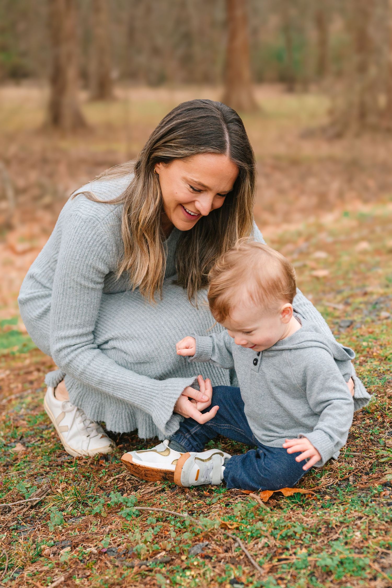 A parent and child share a tender moment while sitting on fallen leaves in an autumn forest setting.