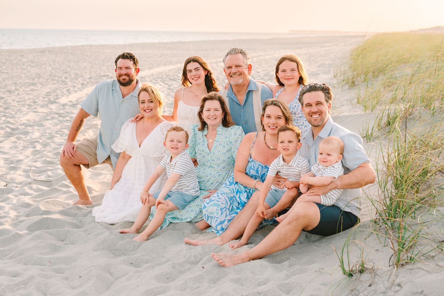 Extended family group sits together on sandy beach during golden hour photoshoot.