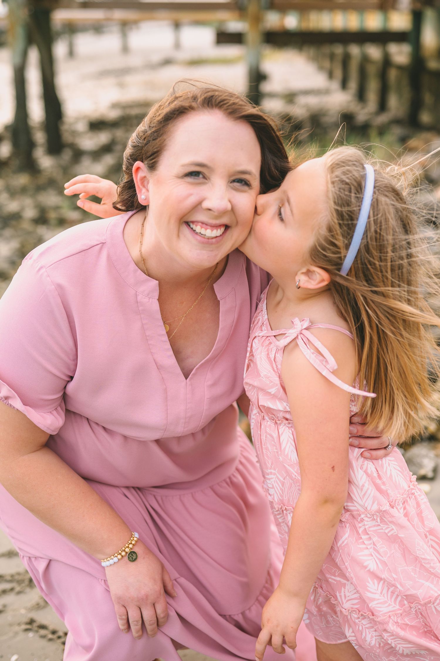 Two people in pink dresses share a joyful moment outdoors with natural lighting and windswept hair.