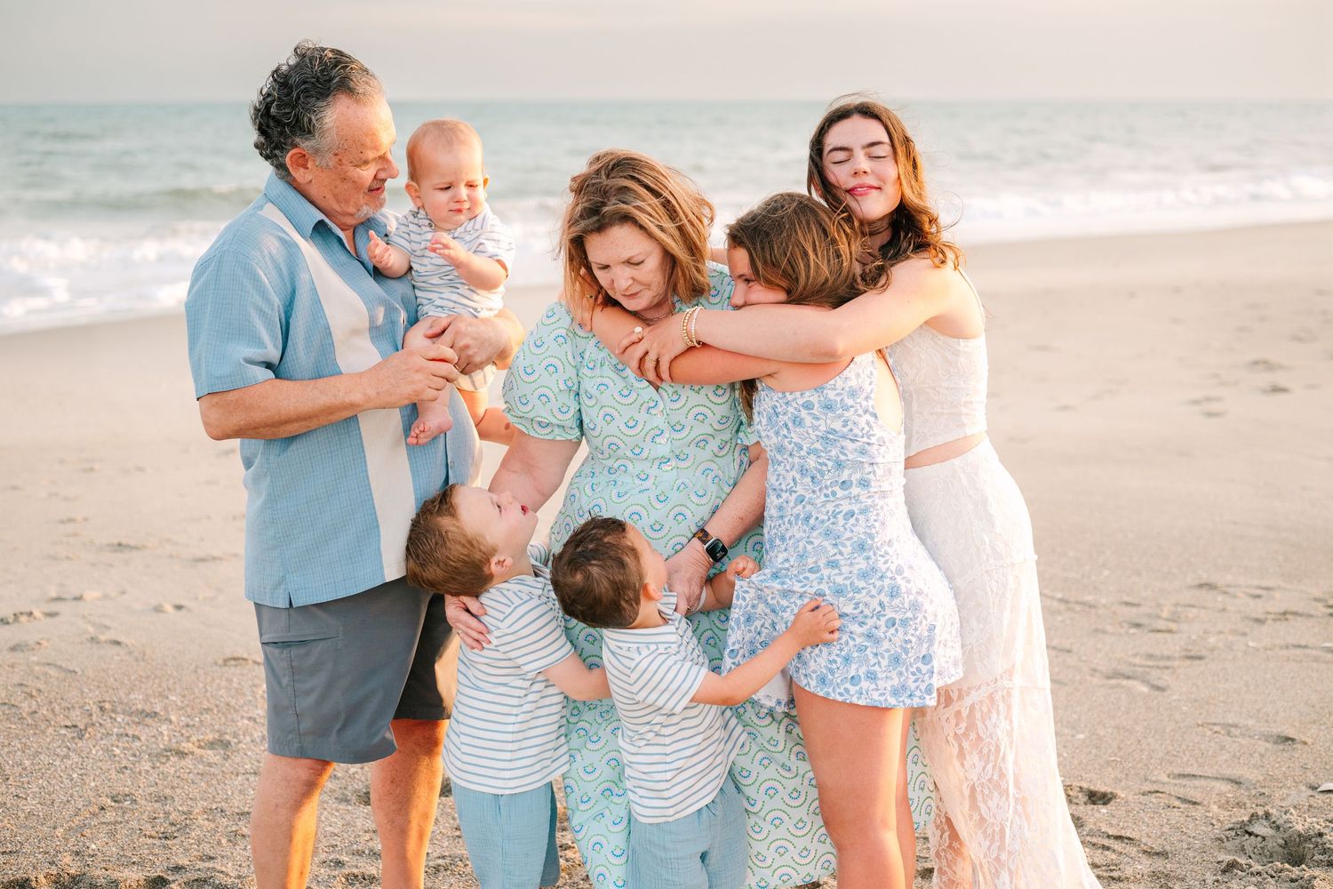 Family enjoying a playful moment together on the beach at sunset with coordinated blue and white outfits.