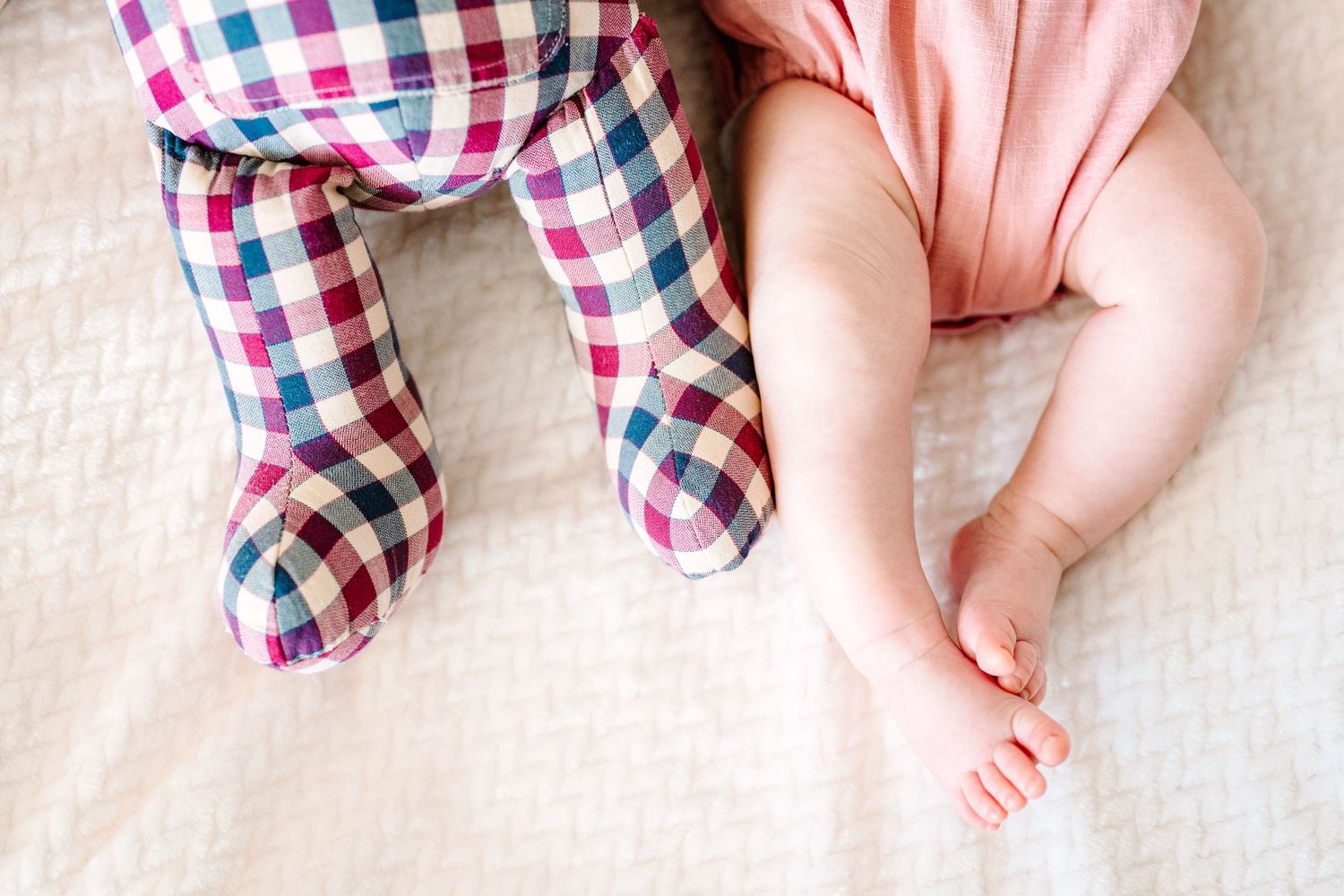 Two baby feet next to plaid patterned pajamas on a white blanket.