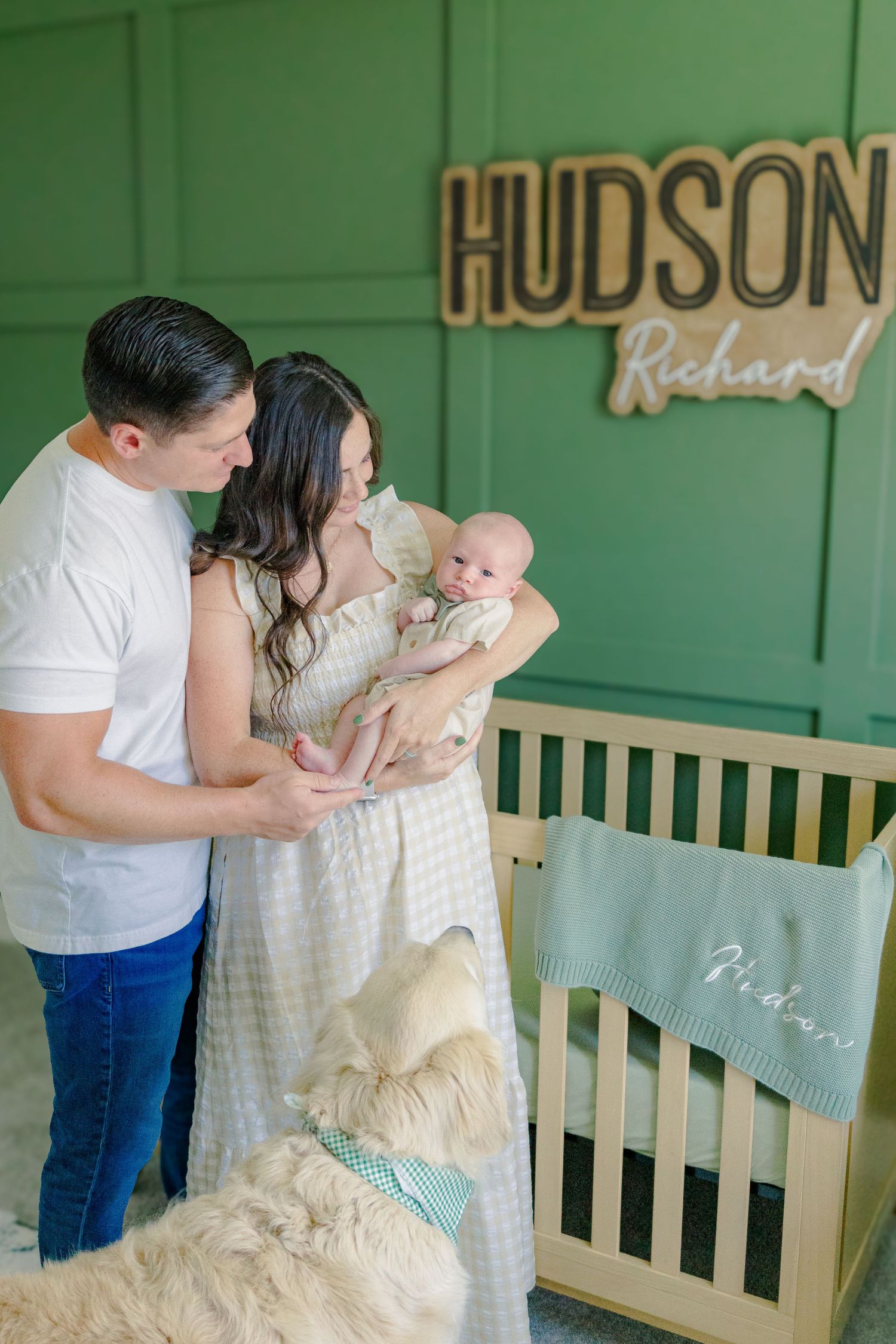 A nursery scene with green walls featuring a wooden crib and custom name sign.