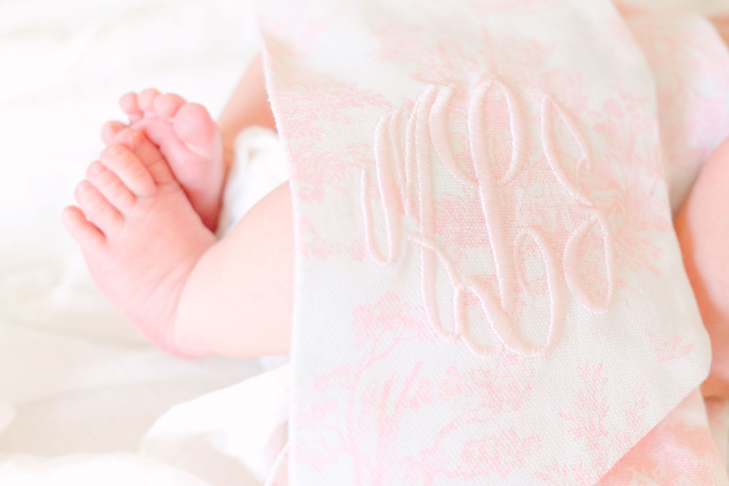 Close up of tiny newborn baby feet against soft pink and white monogrammed fabric.