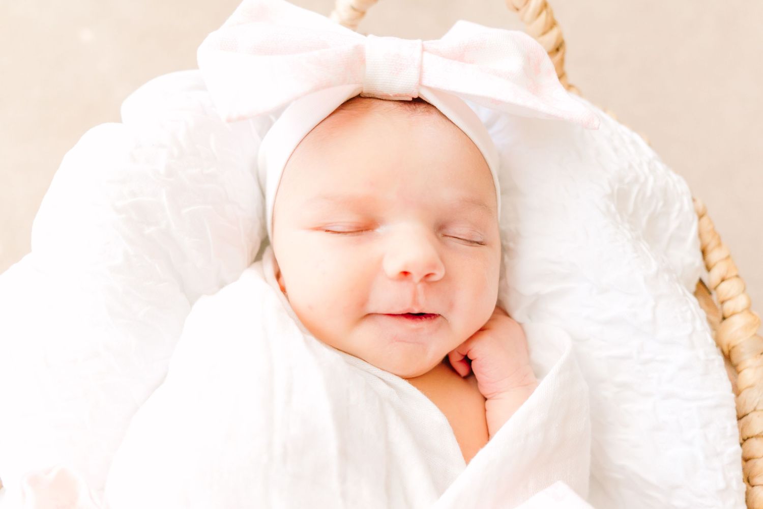 A peaceful newborn sleeping in white wrappings with a large pink bow headband.