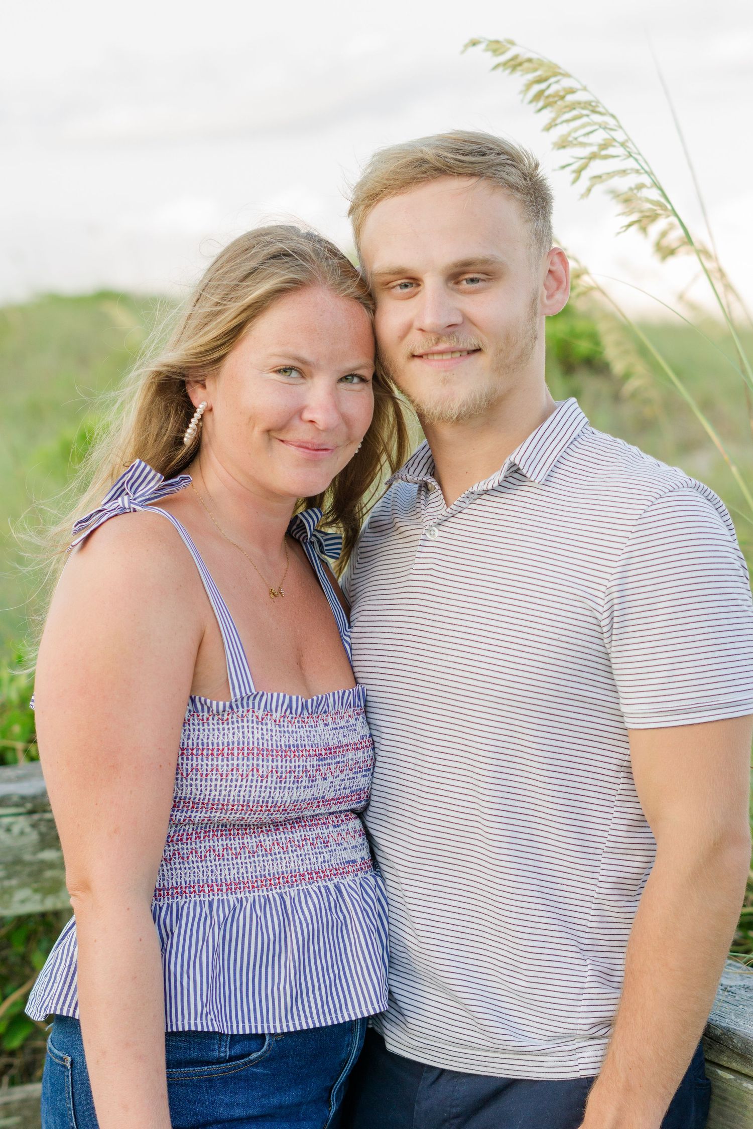 A couple in coordinating striped outfits poses together on a coastal boardwalk.