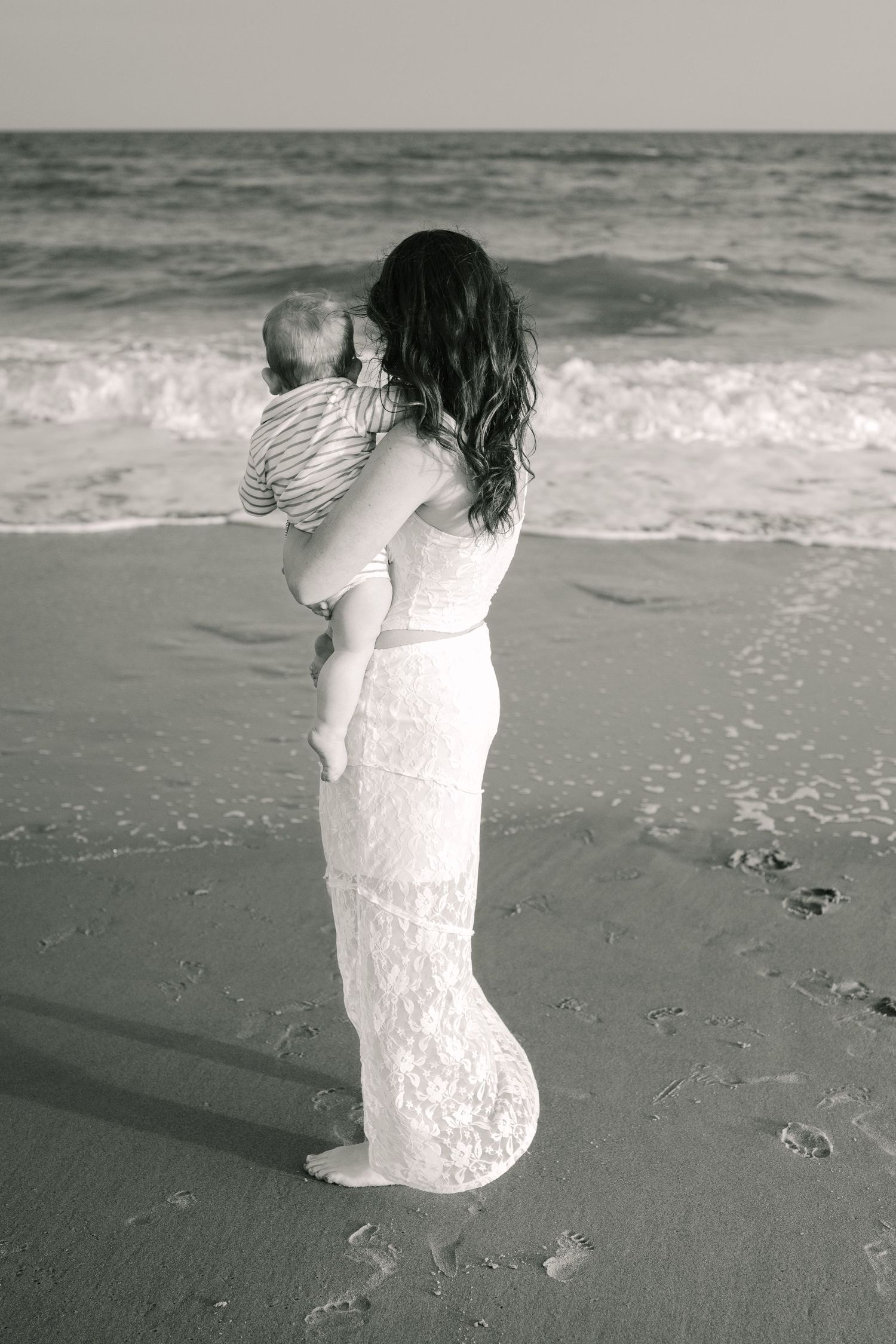 Black and white photo of figure in lace dress holding child on beach.