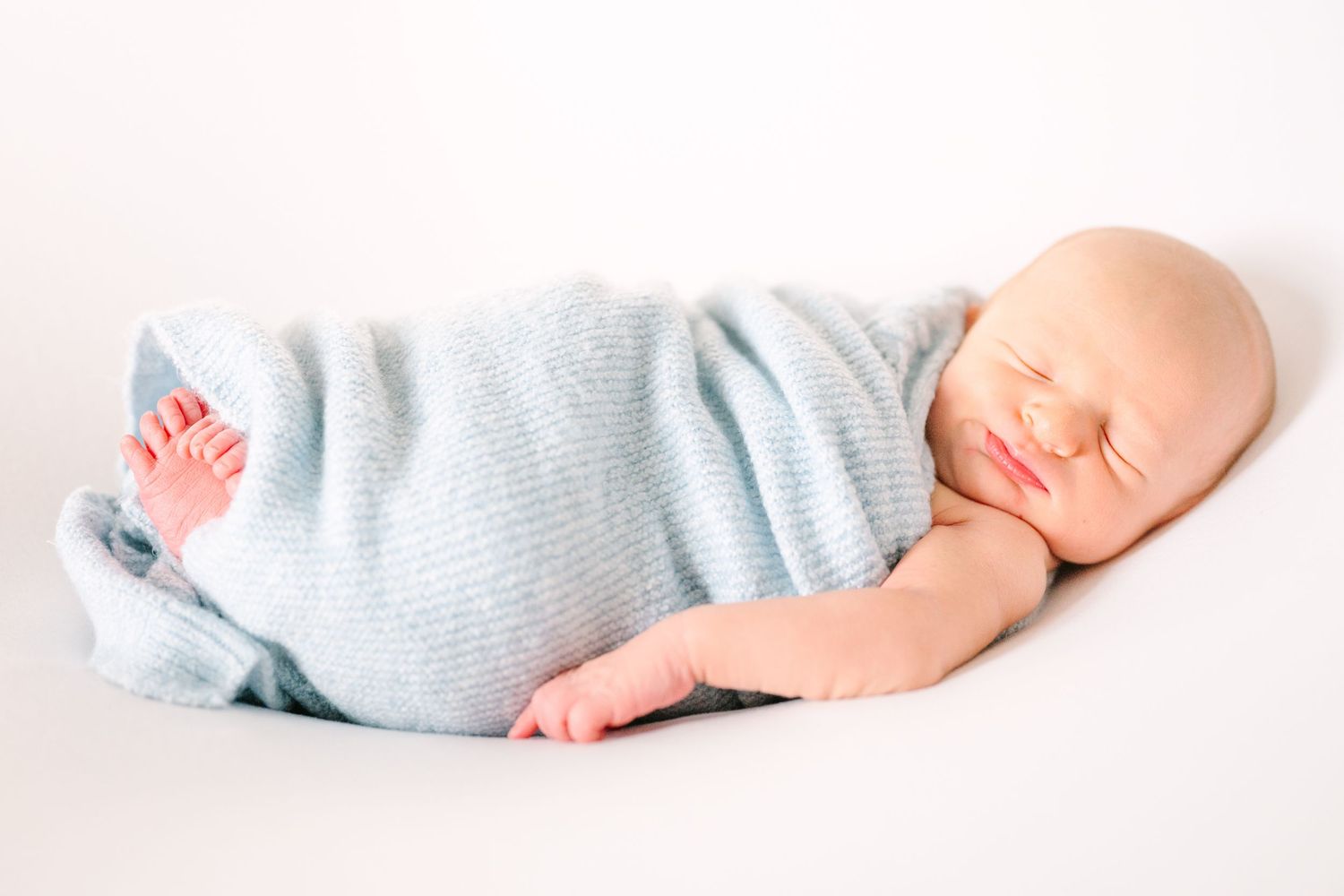 Sleeping newborn in soft blue knit clothing rests on white background during portrait session.
