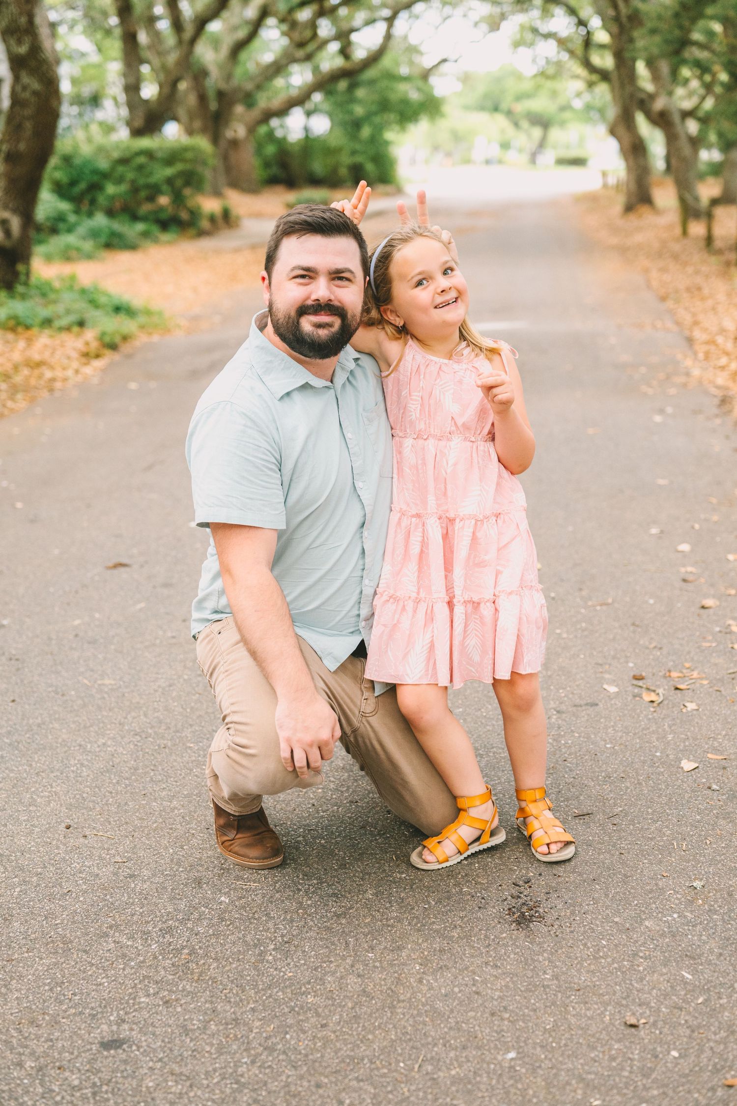 A parent and child pose playfully together on a tree-lined path on an autumn day.