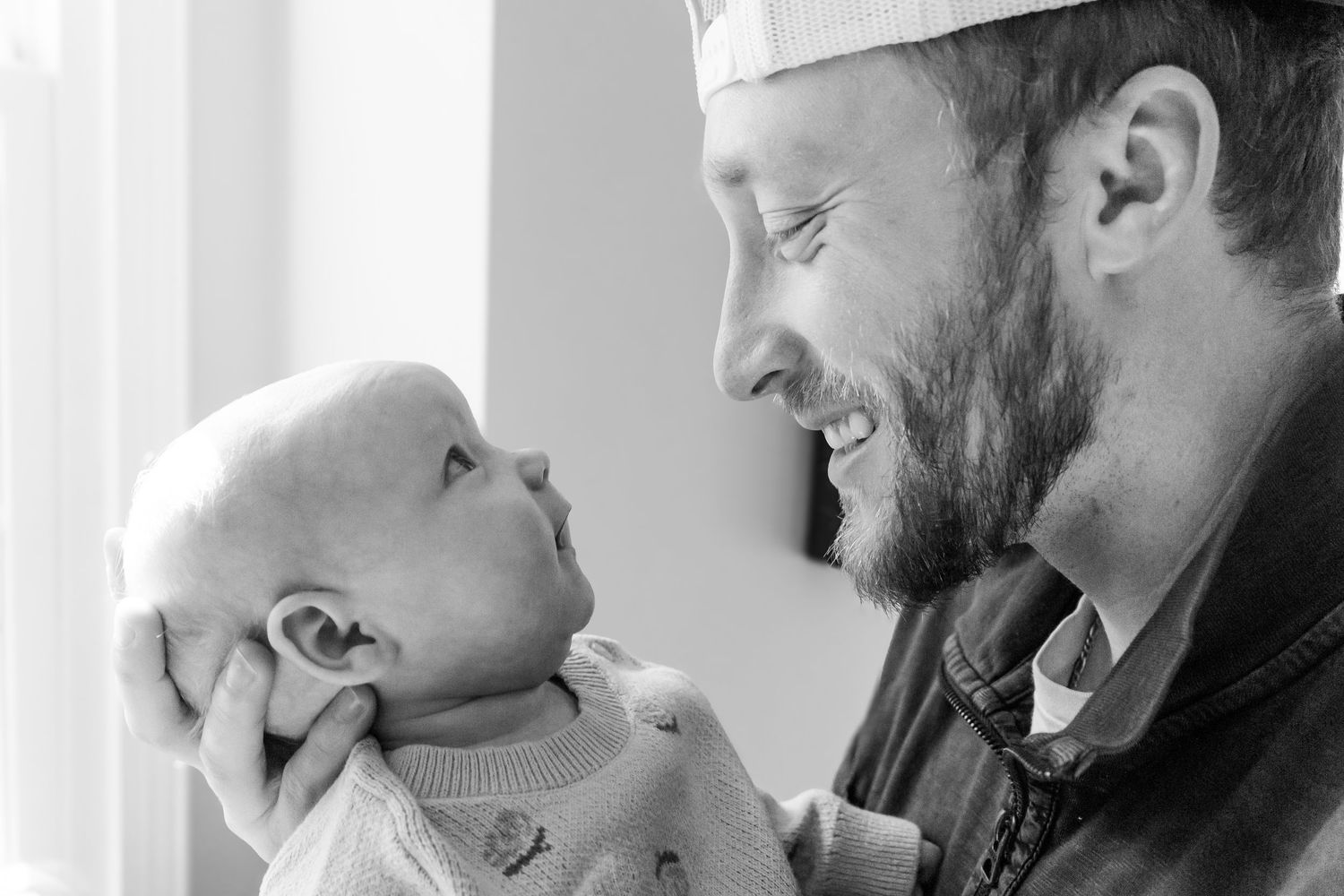 A tender moment between an adult and infant as they gaze at each other in black and white.