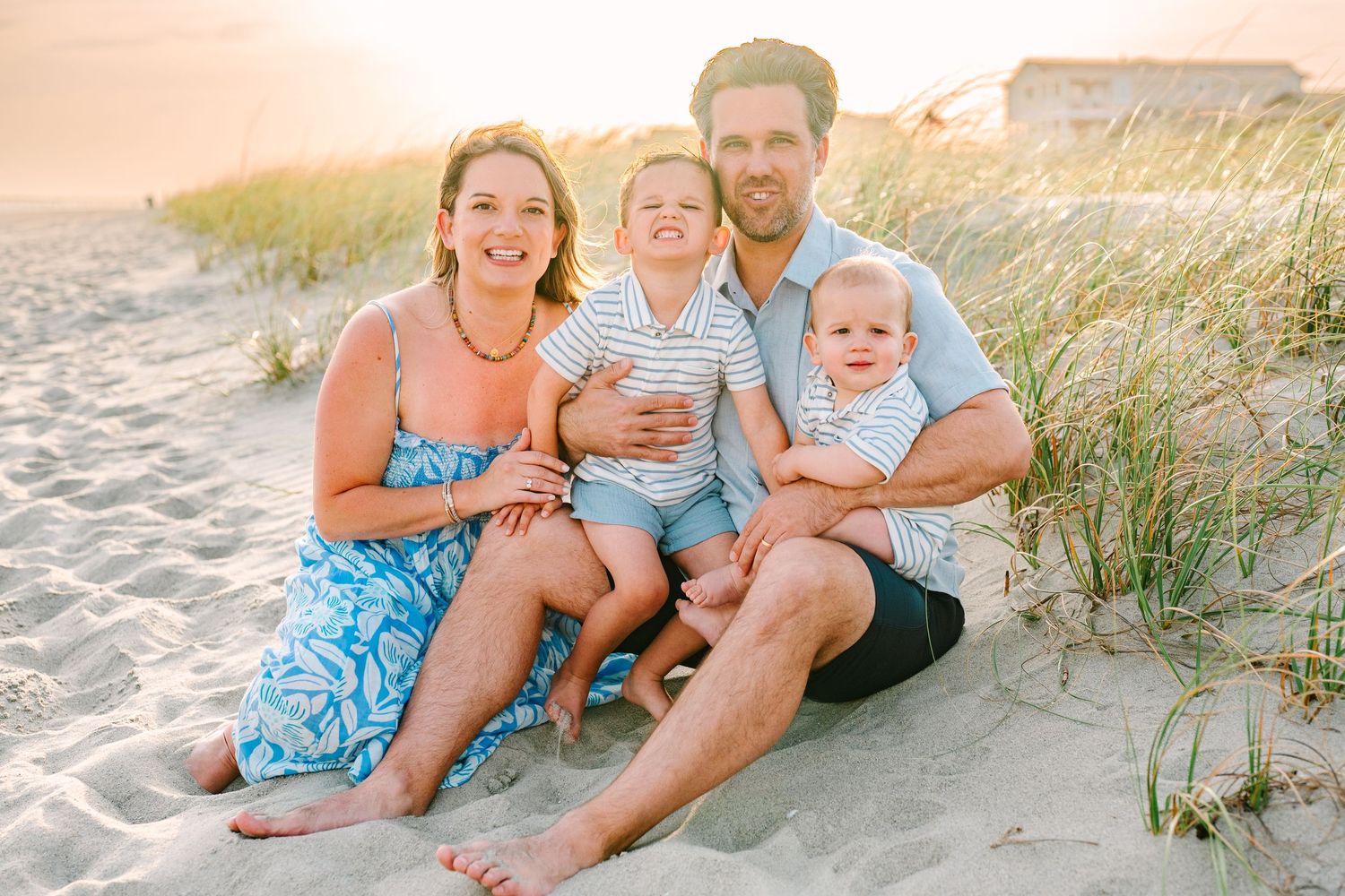 Happy family of four sitting together on sandy beach dunes during golden hour photoshoot.