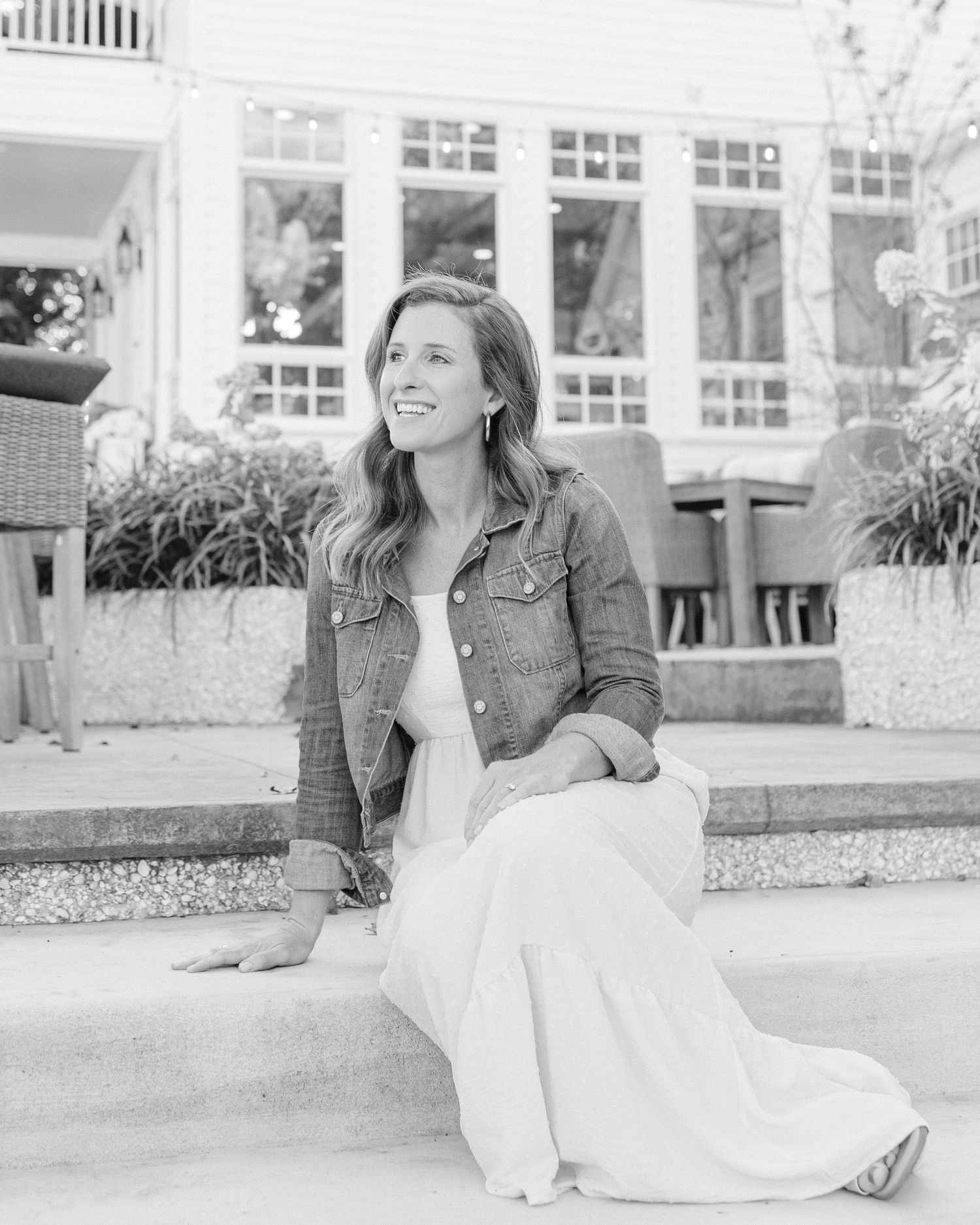 A casual portrait on an outdoor patio featuring someone in a denim jacket and white dress.