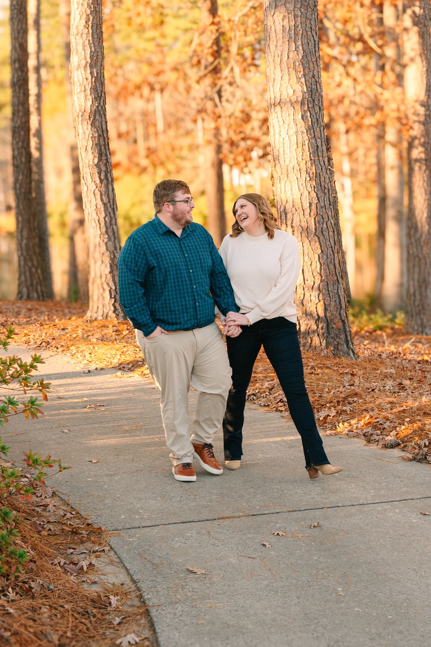A couple shares a playful moment on an autumn path surrounded by golden trees.