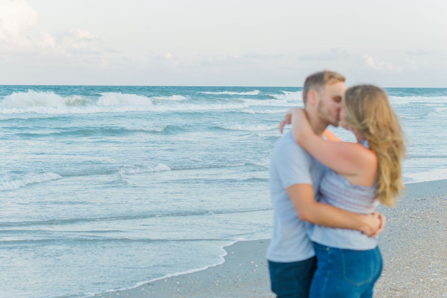 A couple embraces on the beach with waves crashing in the background.