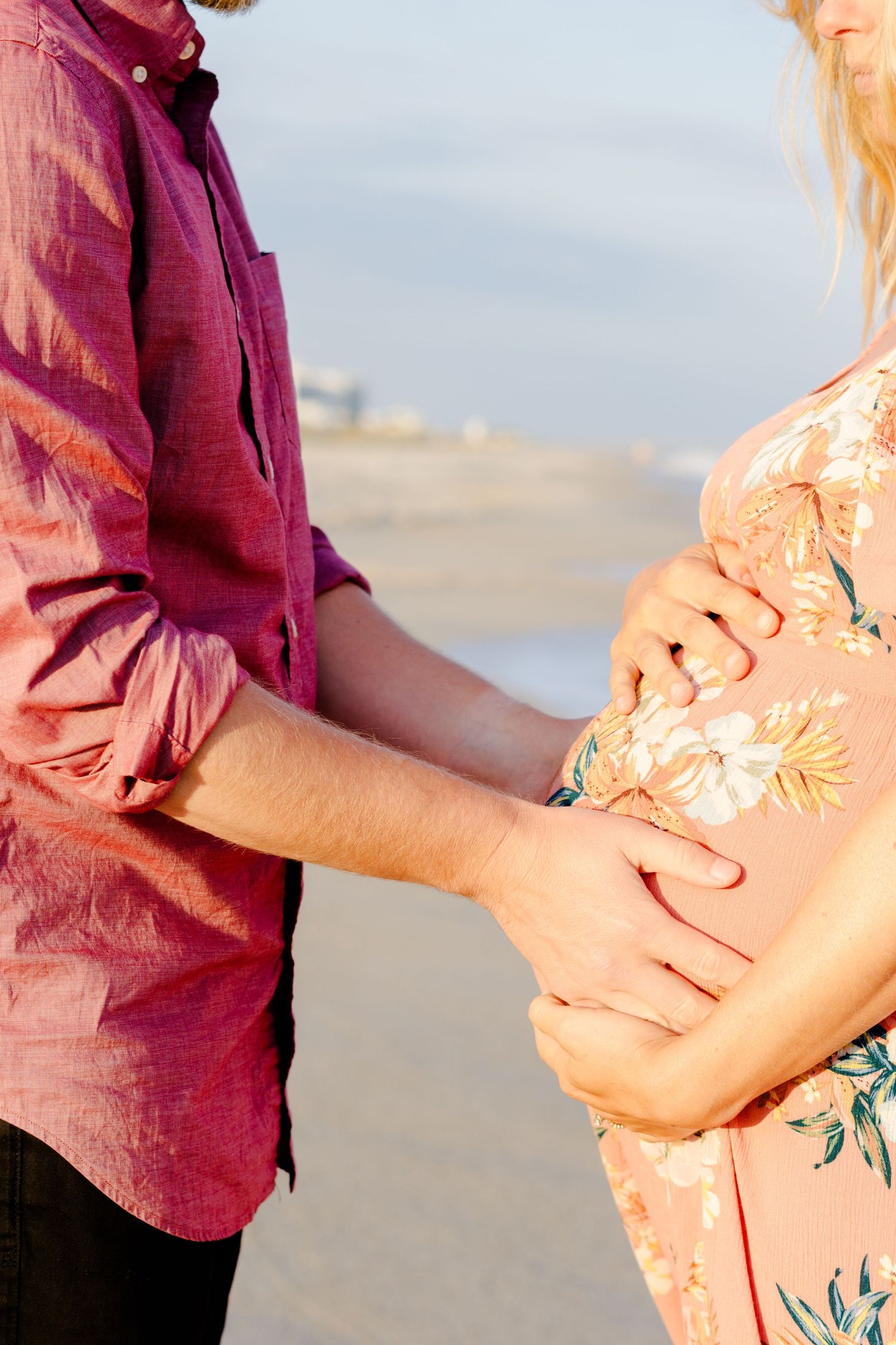 Close-up of hands tenderly cradling pregnant belly on beach during maternity photoshoot.