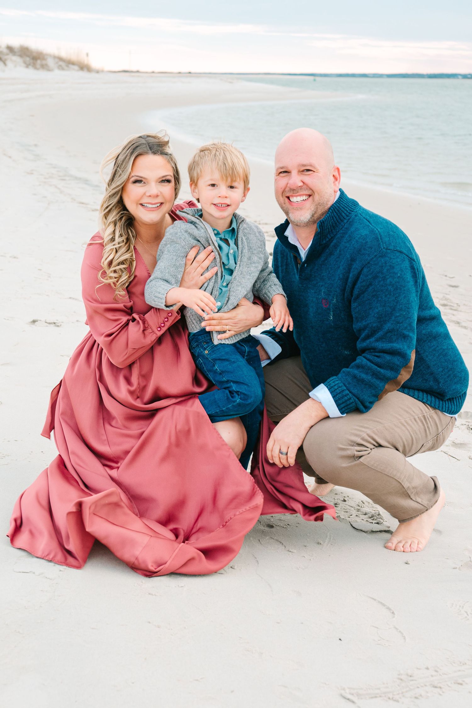 Family portrait on a sunny beach with casual attire and bare feet in the sand.