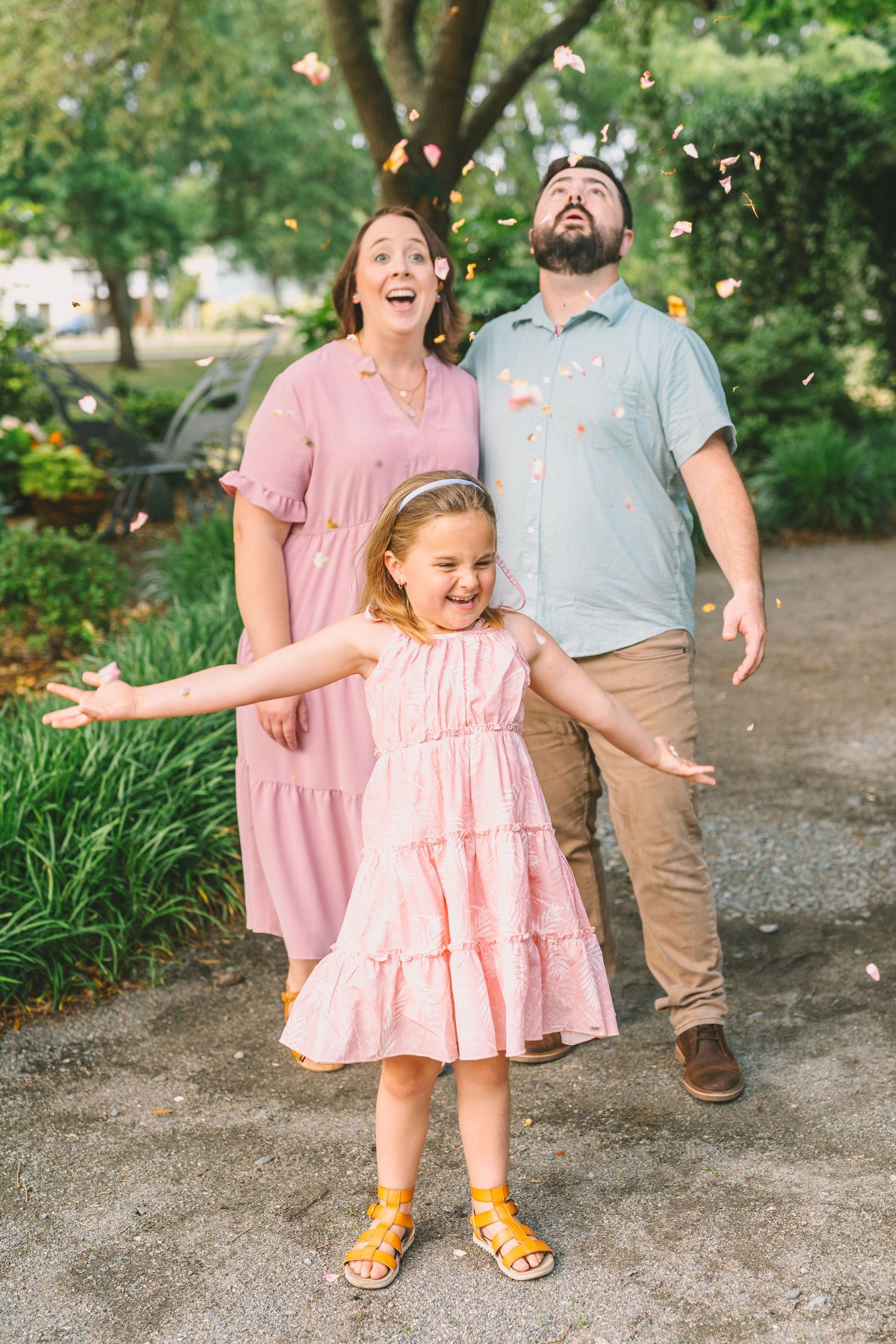 A family enjoys a playful moment together surrounded by flower petals in a lush garden path.
