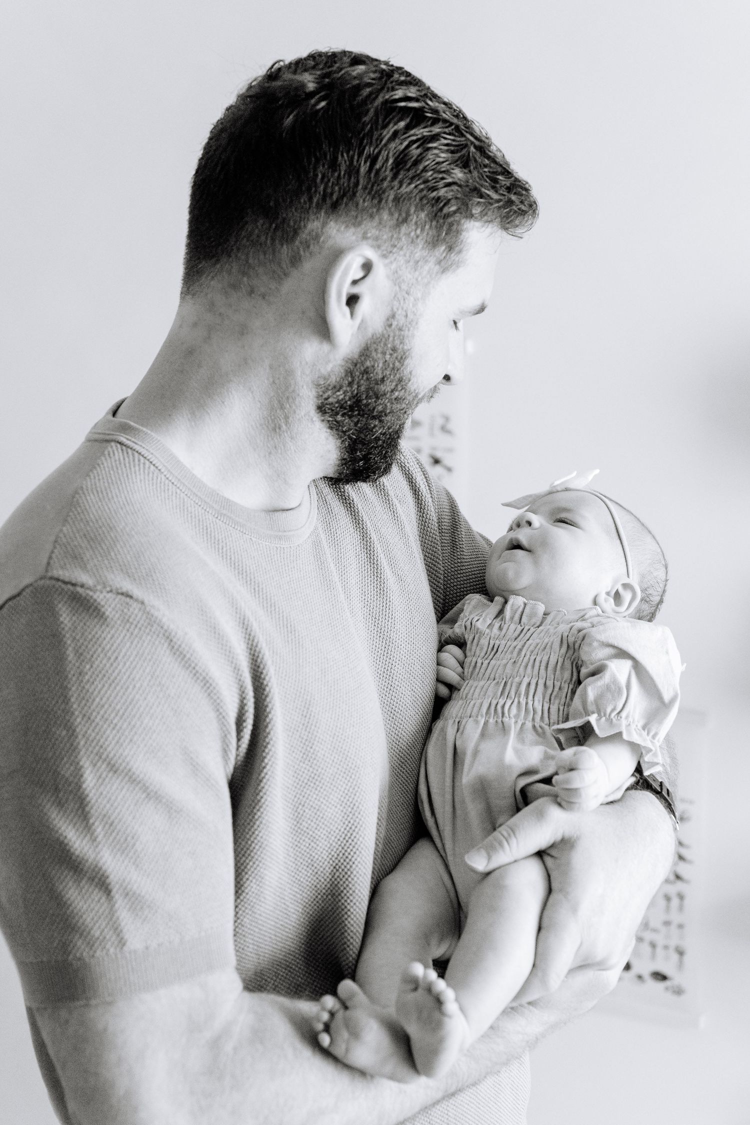 A tender black and white portrait of a parent cradling a tiny newborn baby in their arms.