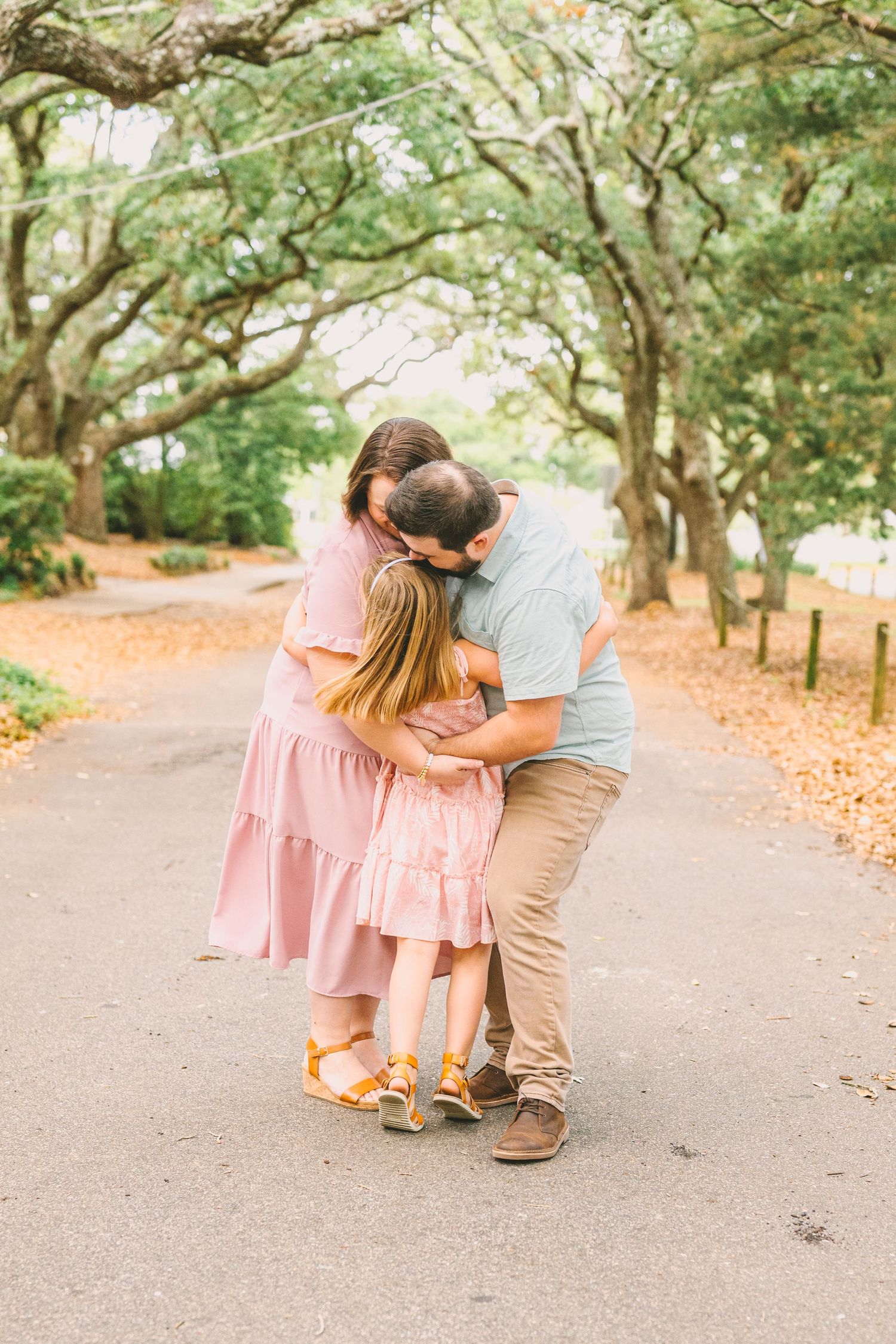 A romantic moment on a tree-lined path with autumn leaves scattered on the ground in a scenic outdoor setting.