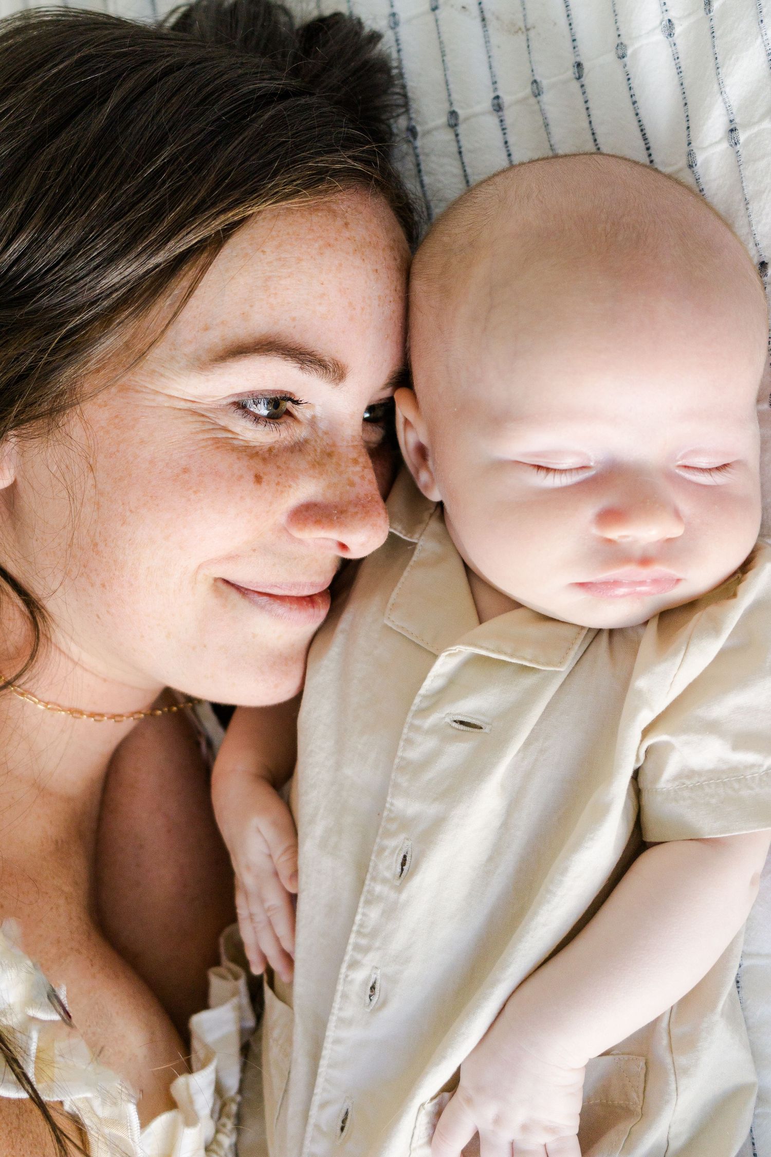 Close-up portrait of mother and sleeping baby on striped bedding.