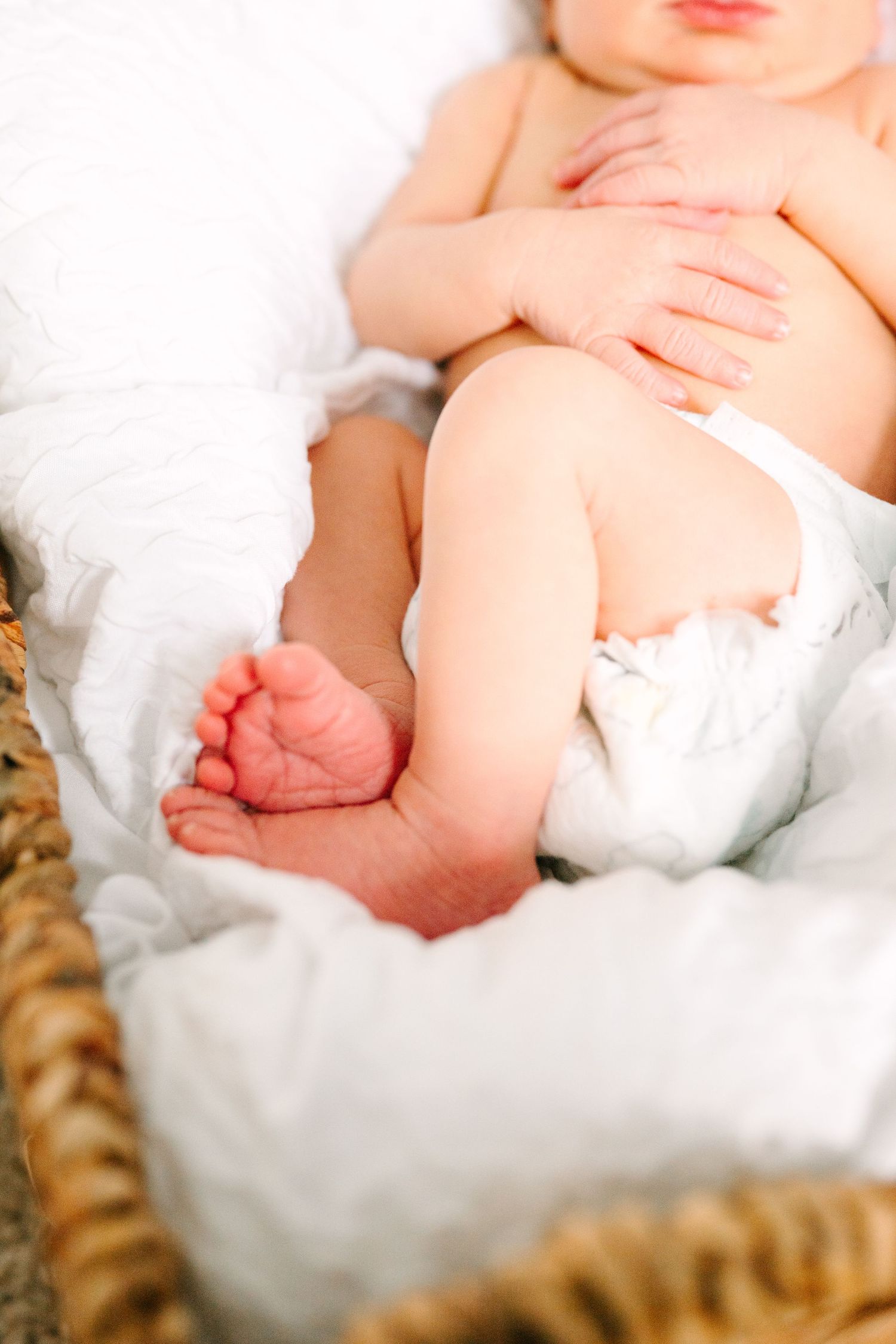 Close up of infant's bare feet and legs resting on soft white blanket in woven basket.