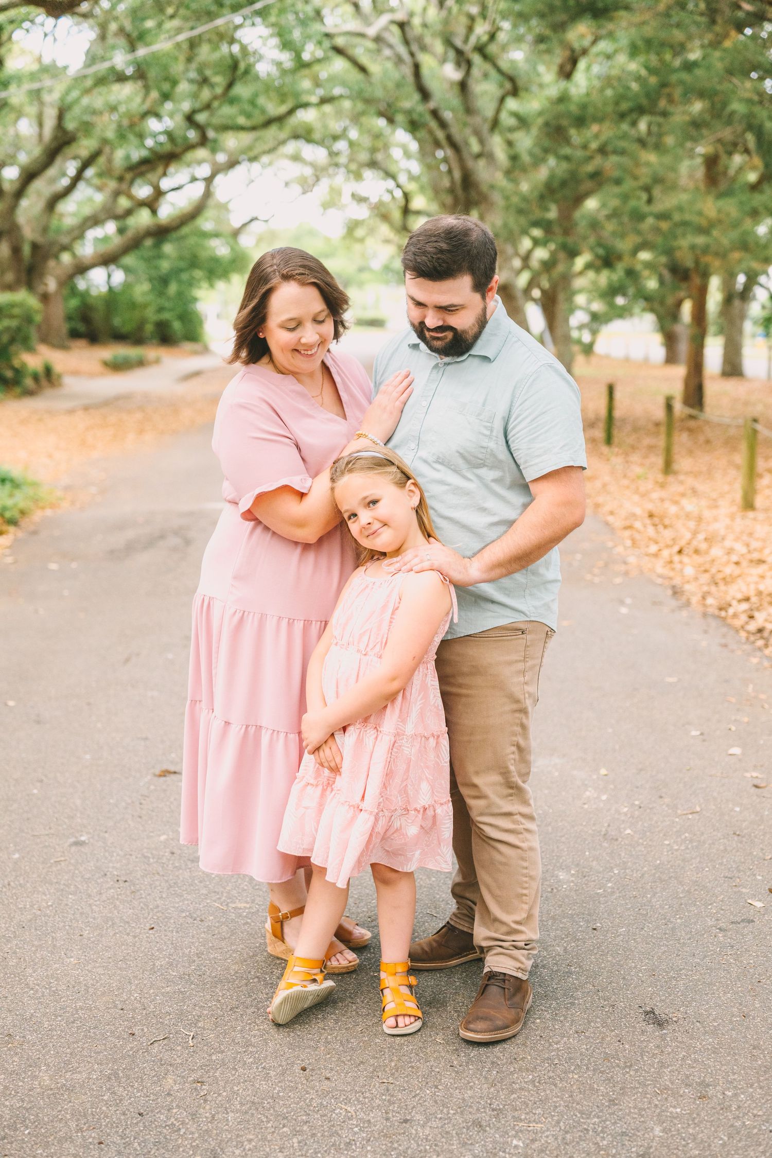 A sweet family moment captured on a tree-lined path in coordinating pink and grey outfits.