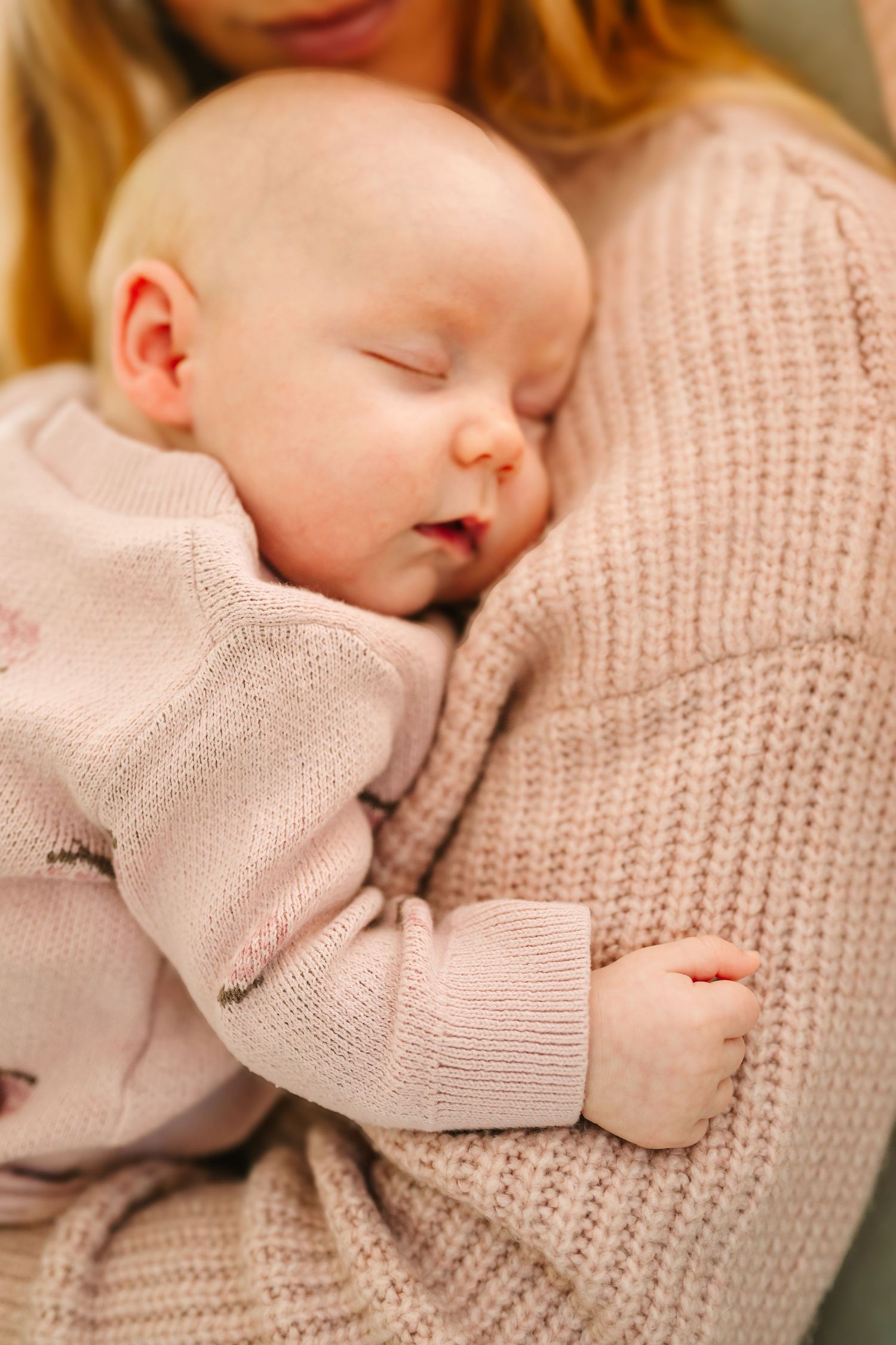 A peacefully sleeping infant in a soft pink sweater rests against a beige knit sweater.