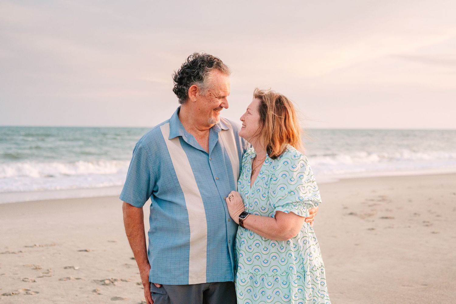 Couple sharing intimate moment on beach at sunset wearing coordinating blue outfits.