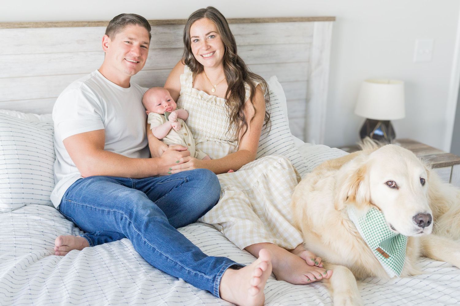 Family relaxes on bed with their baby and white dog wearing bandana.