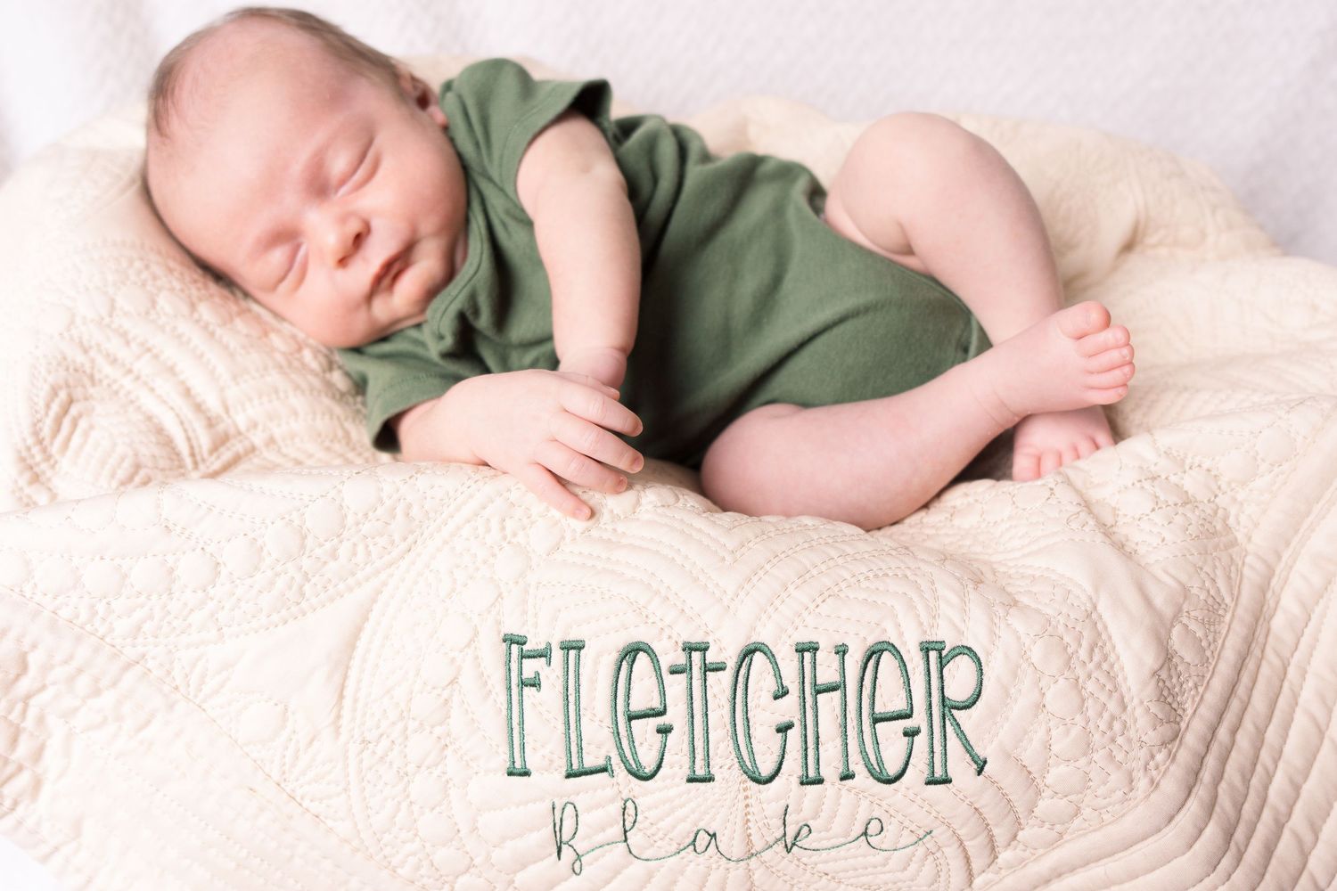 Sleeping newborn in sage green outfit lies on cream textured blanket with name Fletcher displayed below.