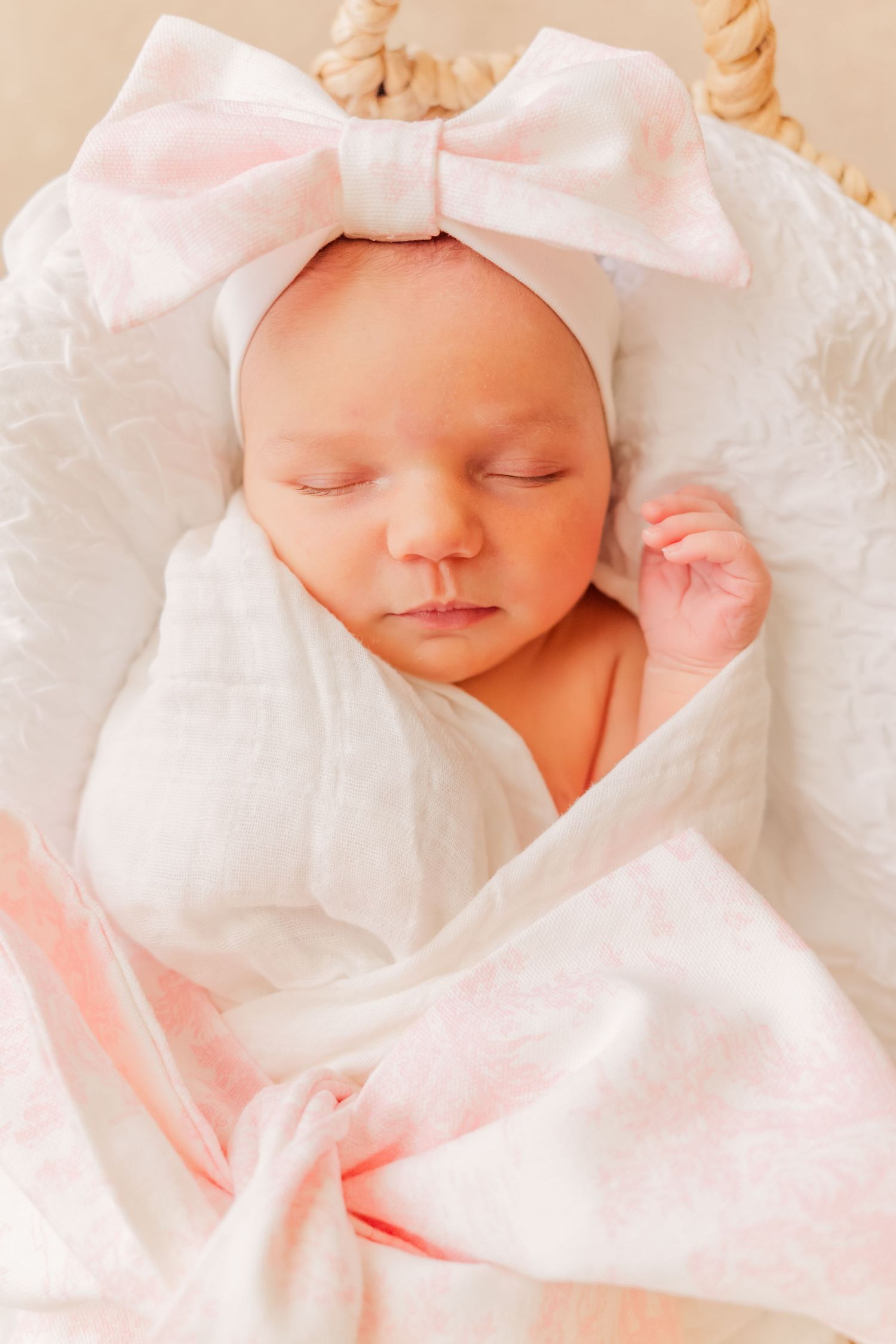 Sleeping newborn wrapped in soft white fabric wearing a pink bow headband.
