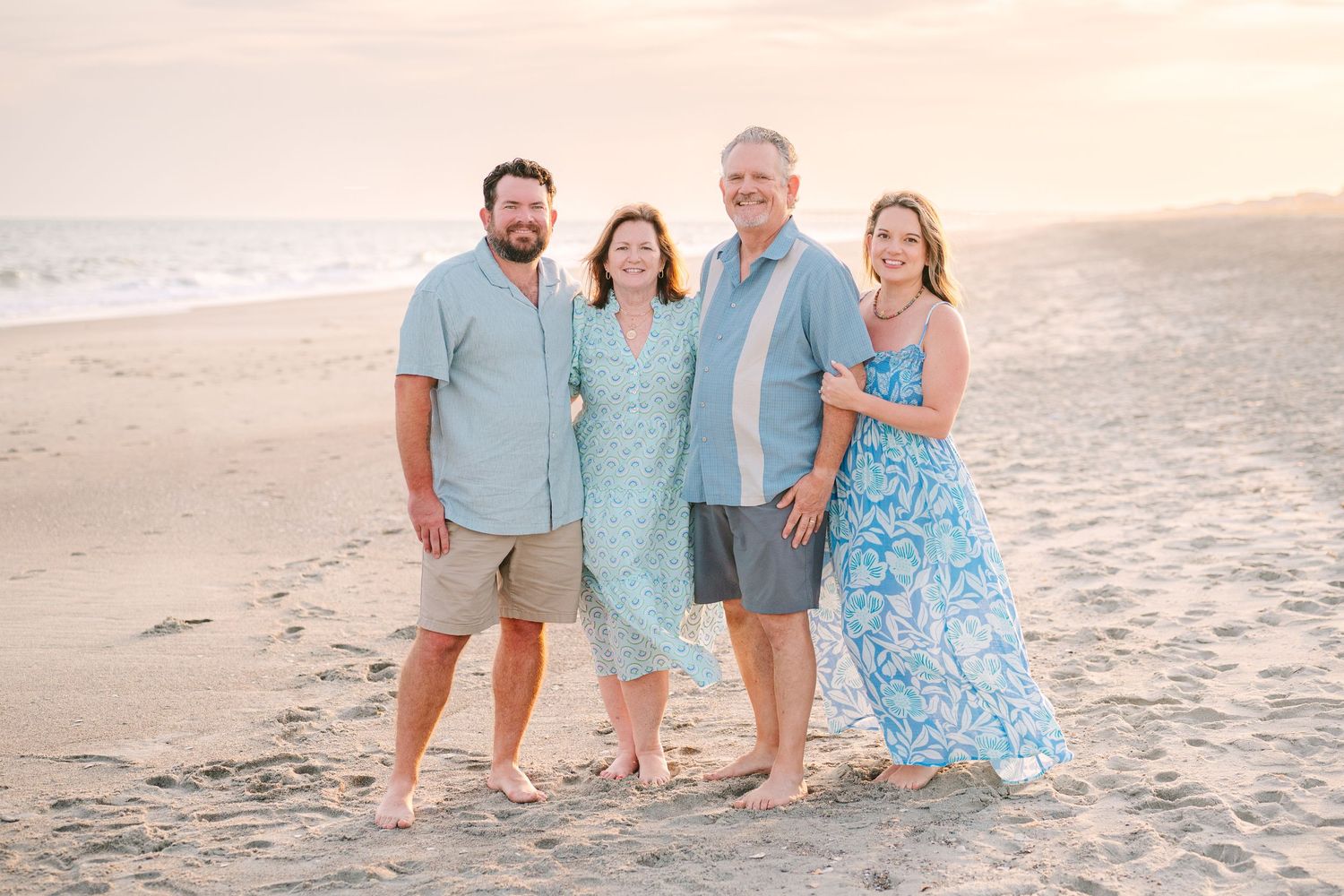 Two couples pose together on the beach wearing coordinating shades of blue and white.