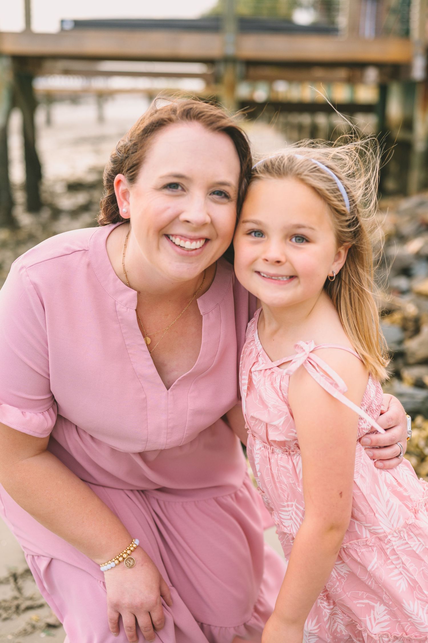 A sweet portrait of two people in matching pink dresses posed by the water.