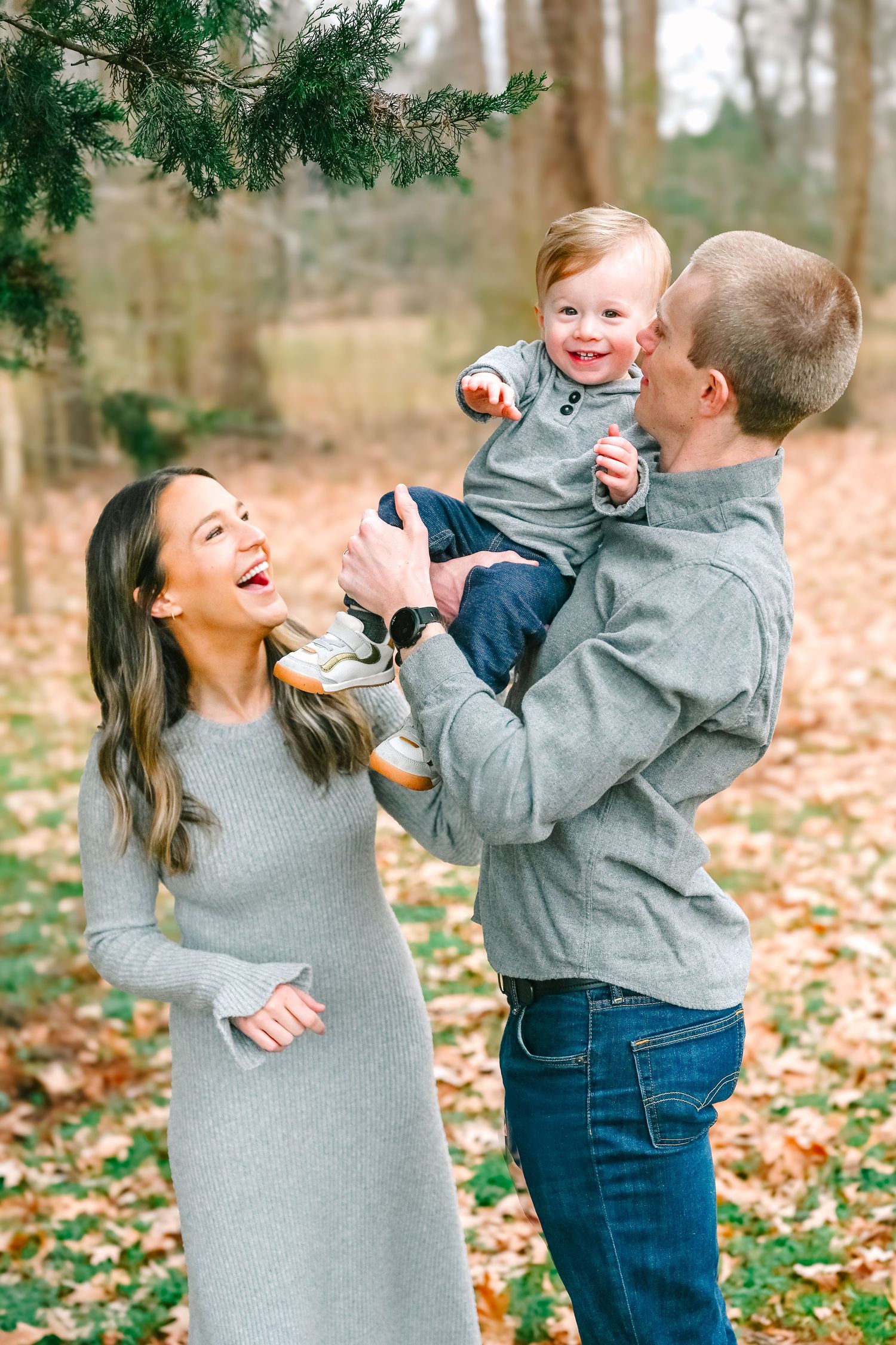 Joyful family playing together outdoors on an autumn day with fallen leaves in a wooded setting.