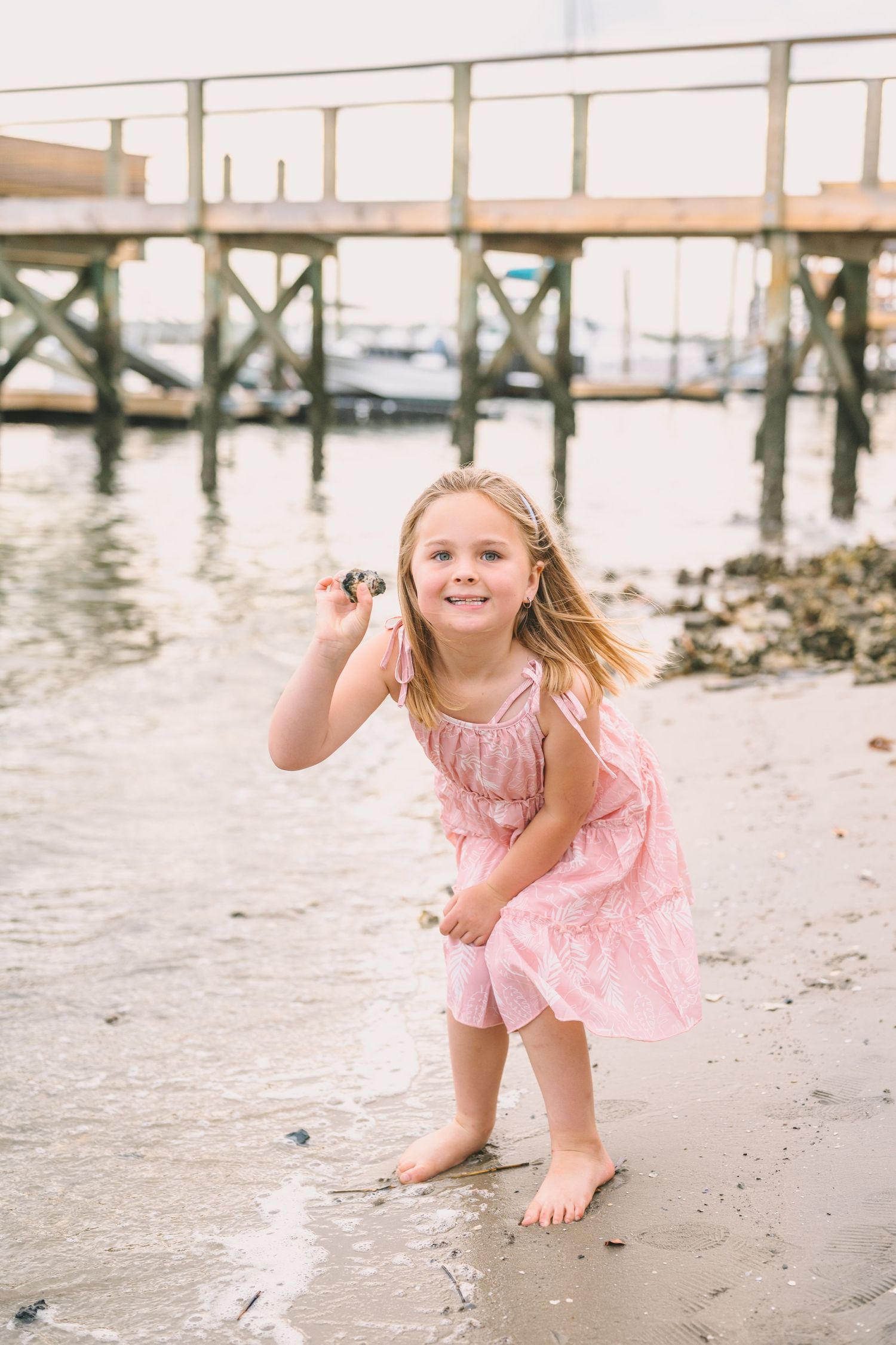 A child plays happily on a beach near a wooden pier during golden hour.