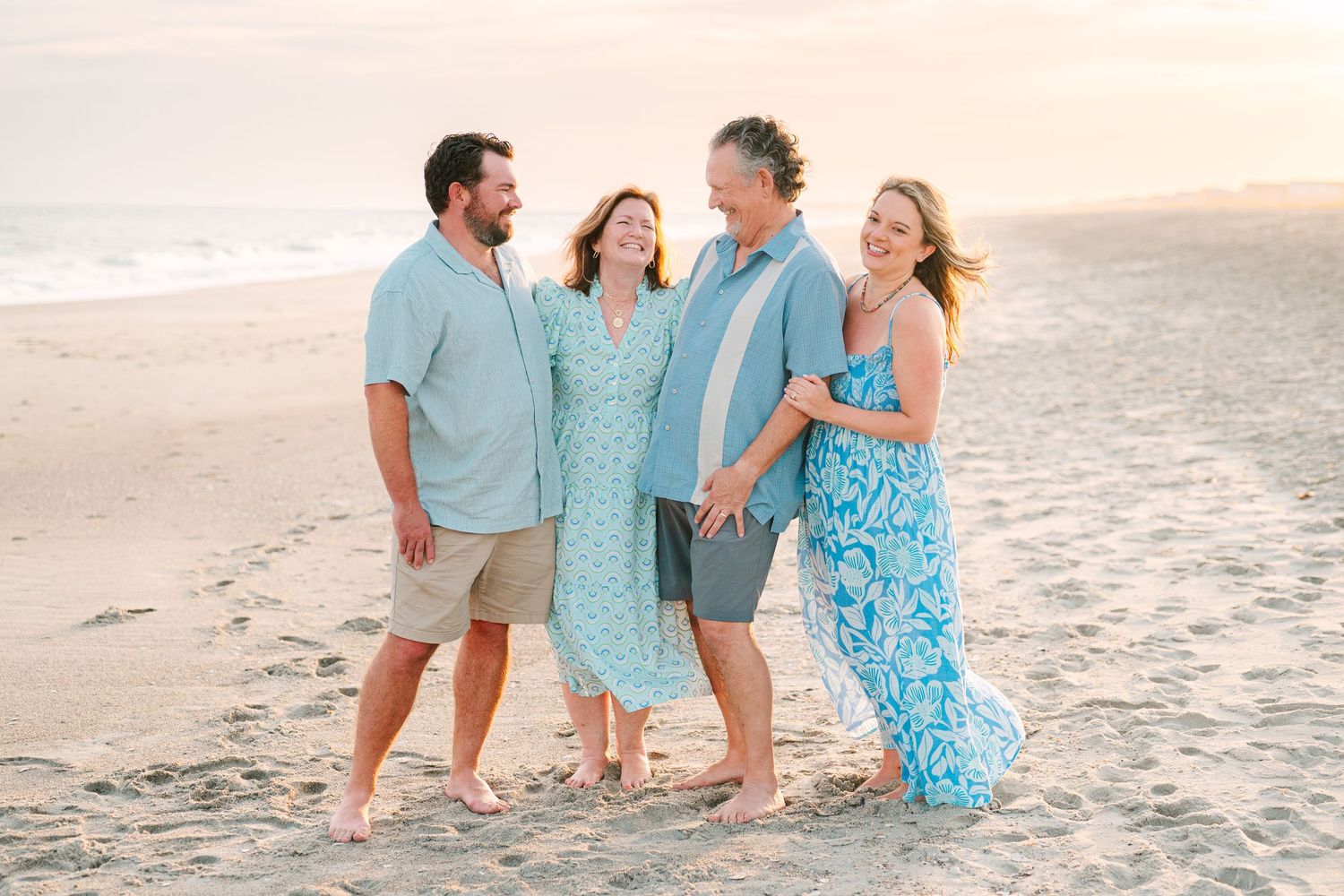Two couples laughing together on beach wearing coordinated blue and white outfits.