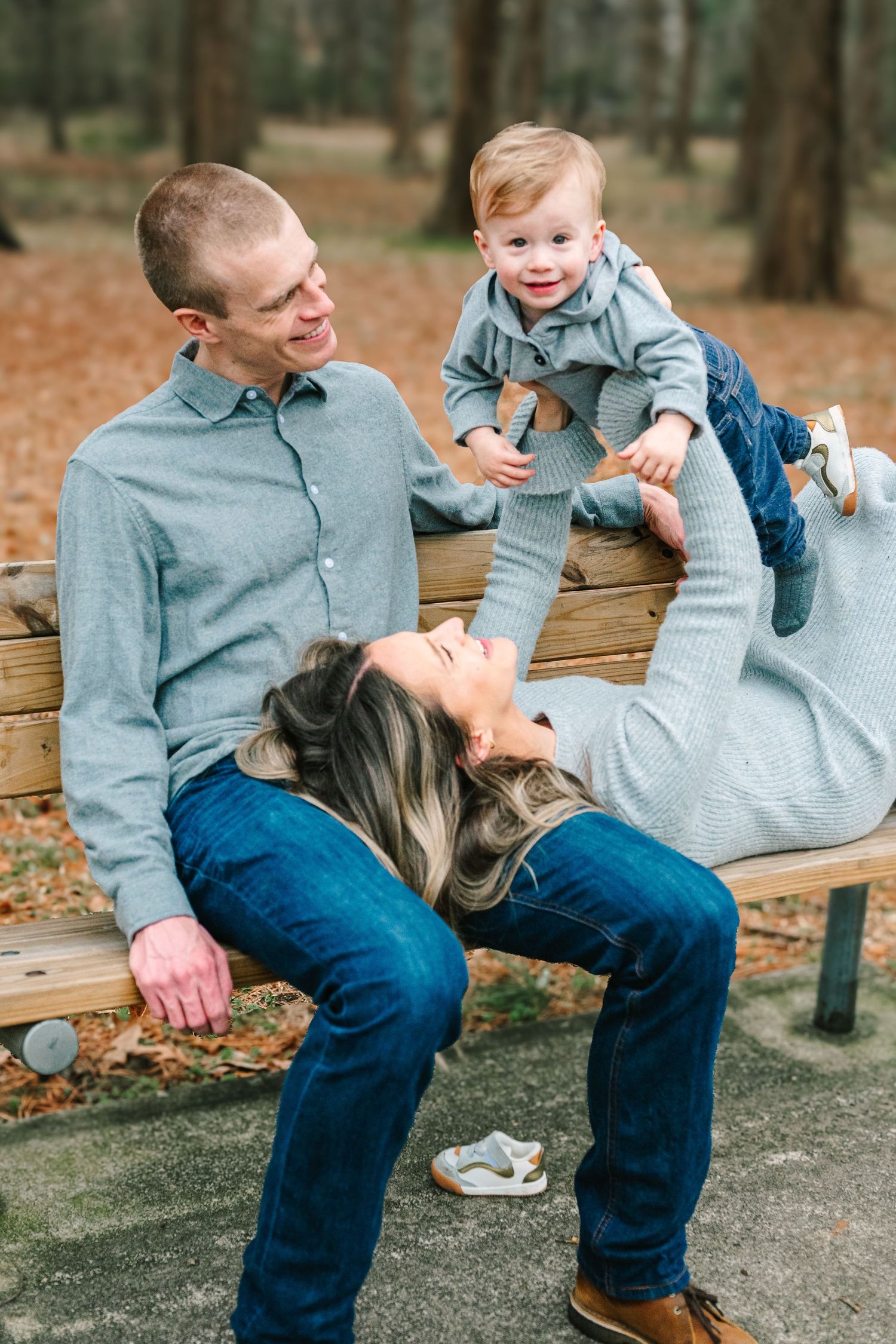 Family plays together and laughs on a wooden bench in an autumn forest park setting.