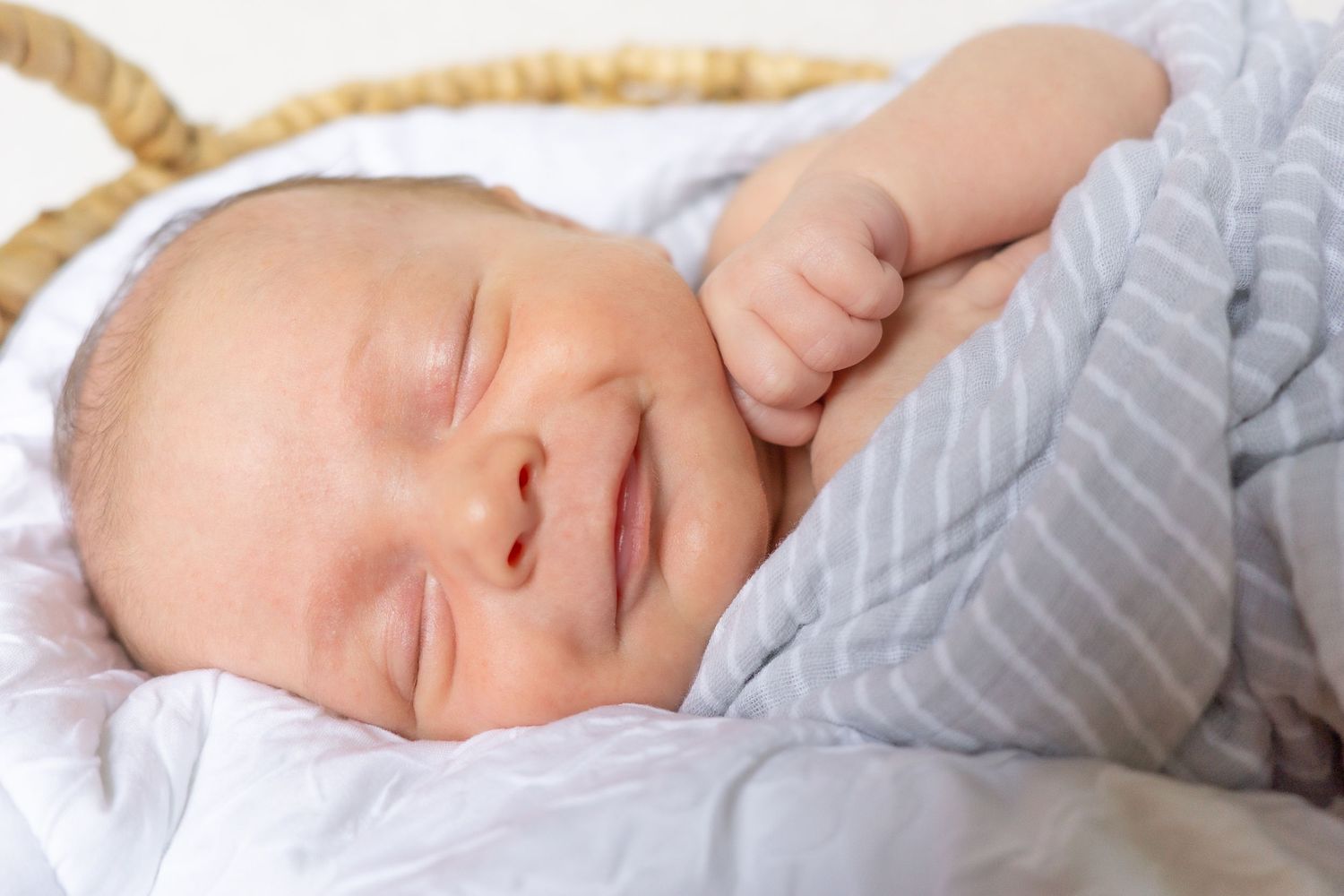 Peaceful sleeping newborn wrapped in striped gray swaddle blanket.
