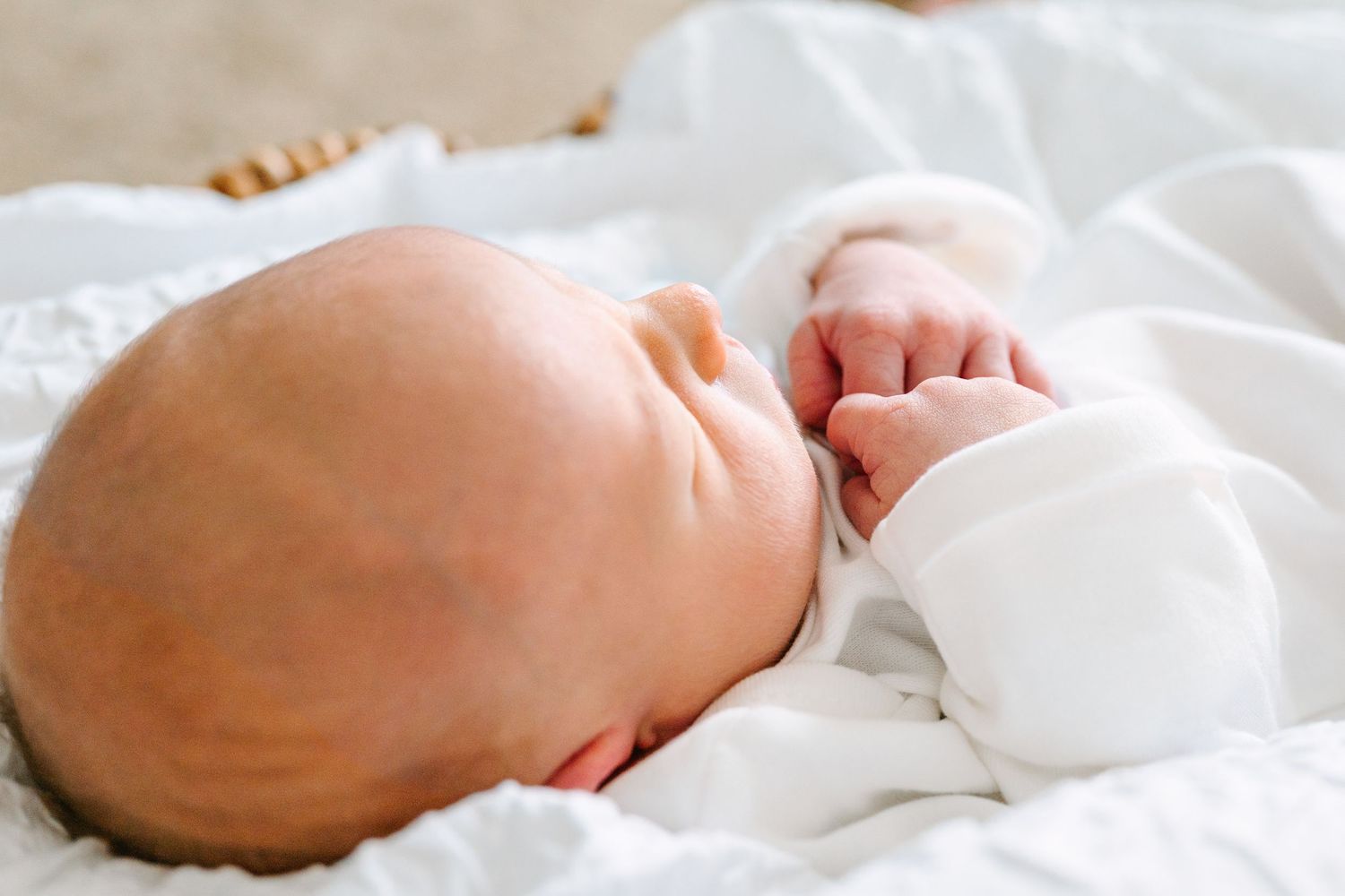 Close-up of sleeping newborn wearing white against soft white bedding.