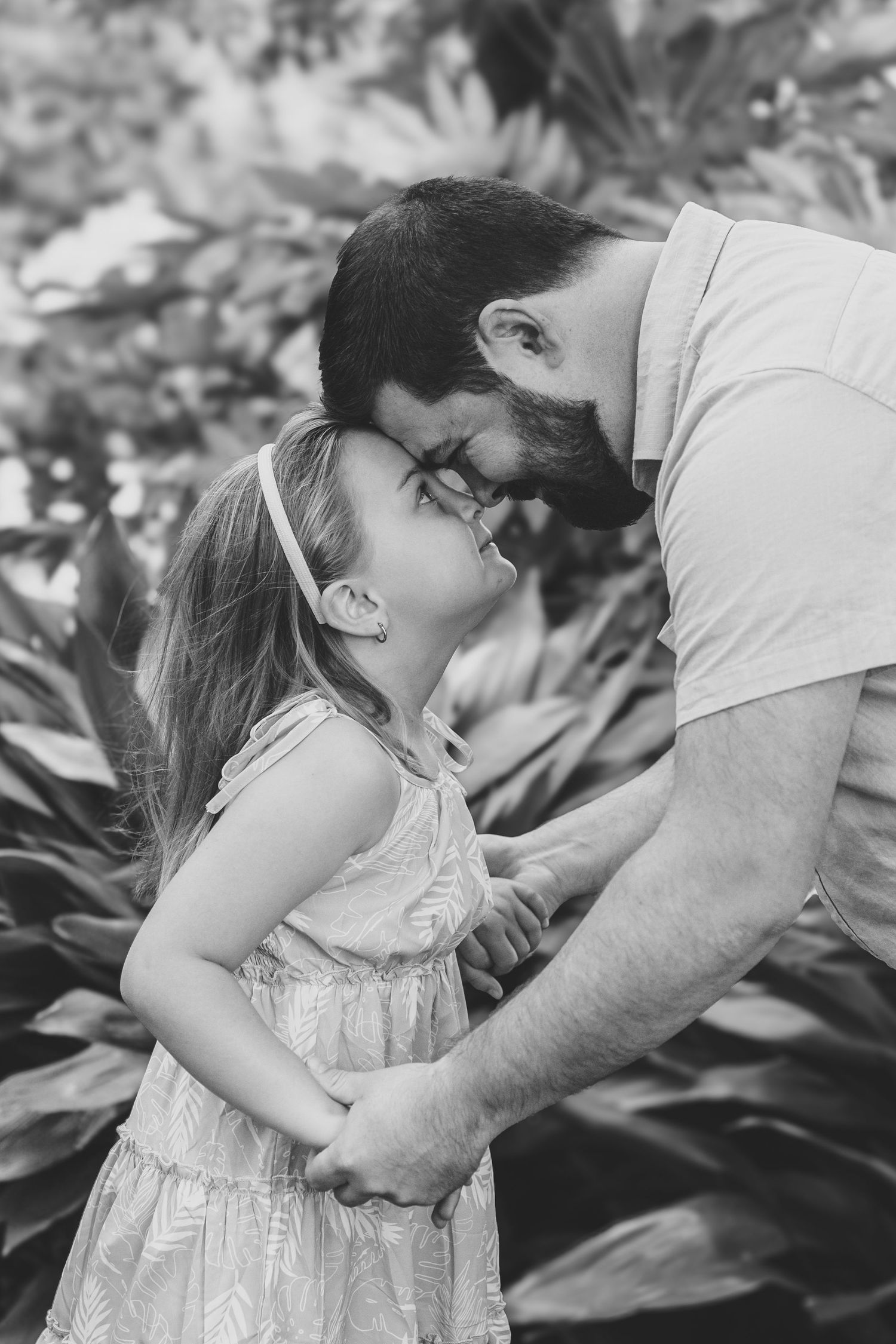 A tender black and white portrait shows a close embrace between two people outdoors among foliage.