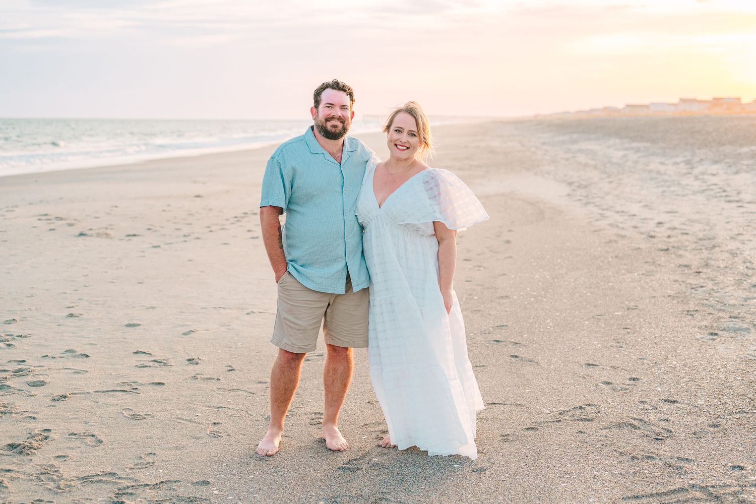 Couple poses together on empty beach at sunset wearing coordinated blue and white outfits.