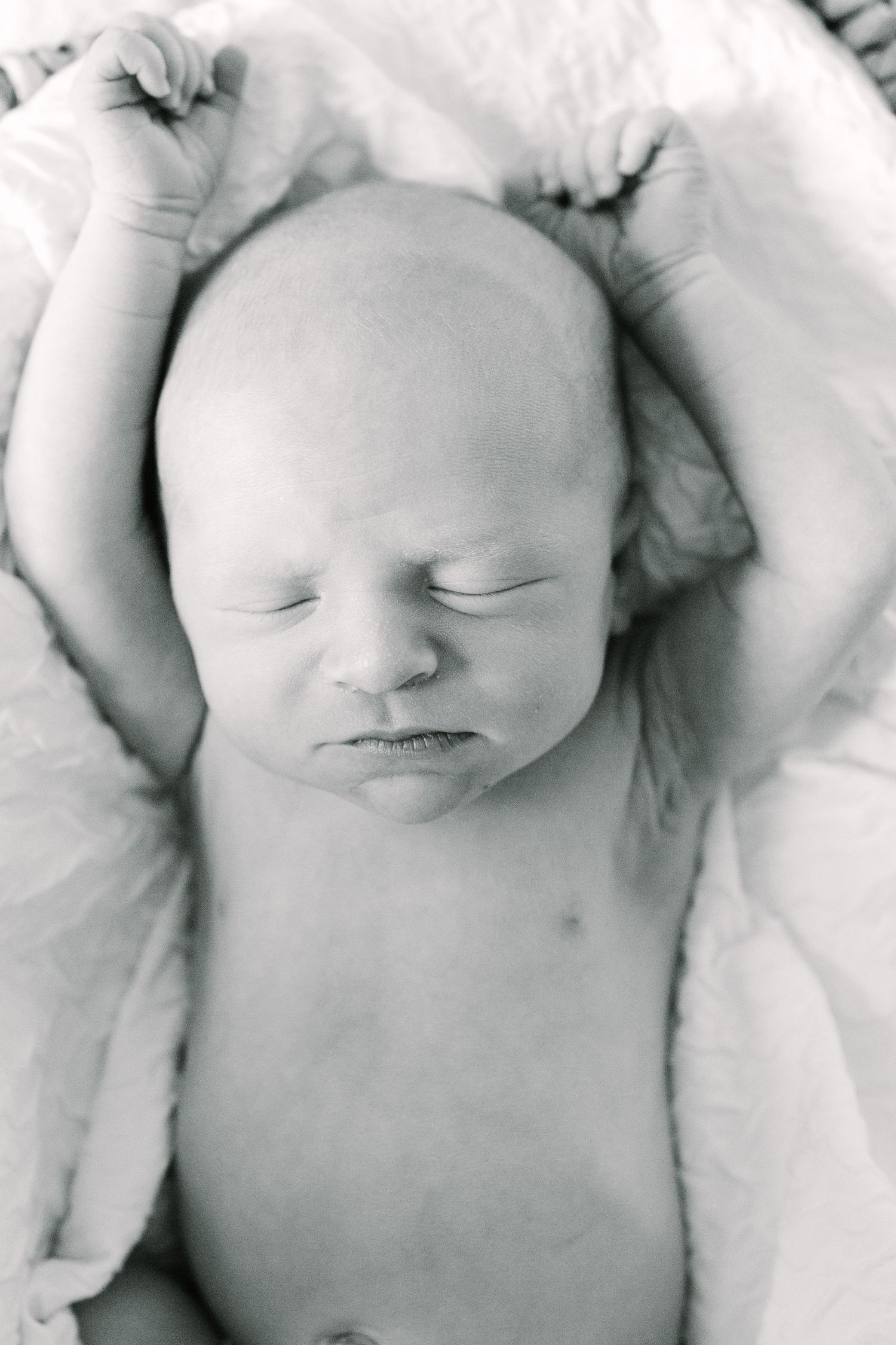 Black and white photograph of a sleeping newborn baby stretching arms on white blanket.
