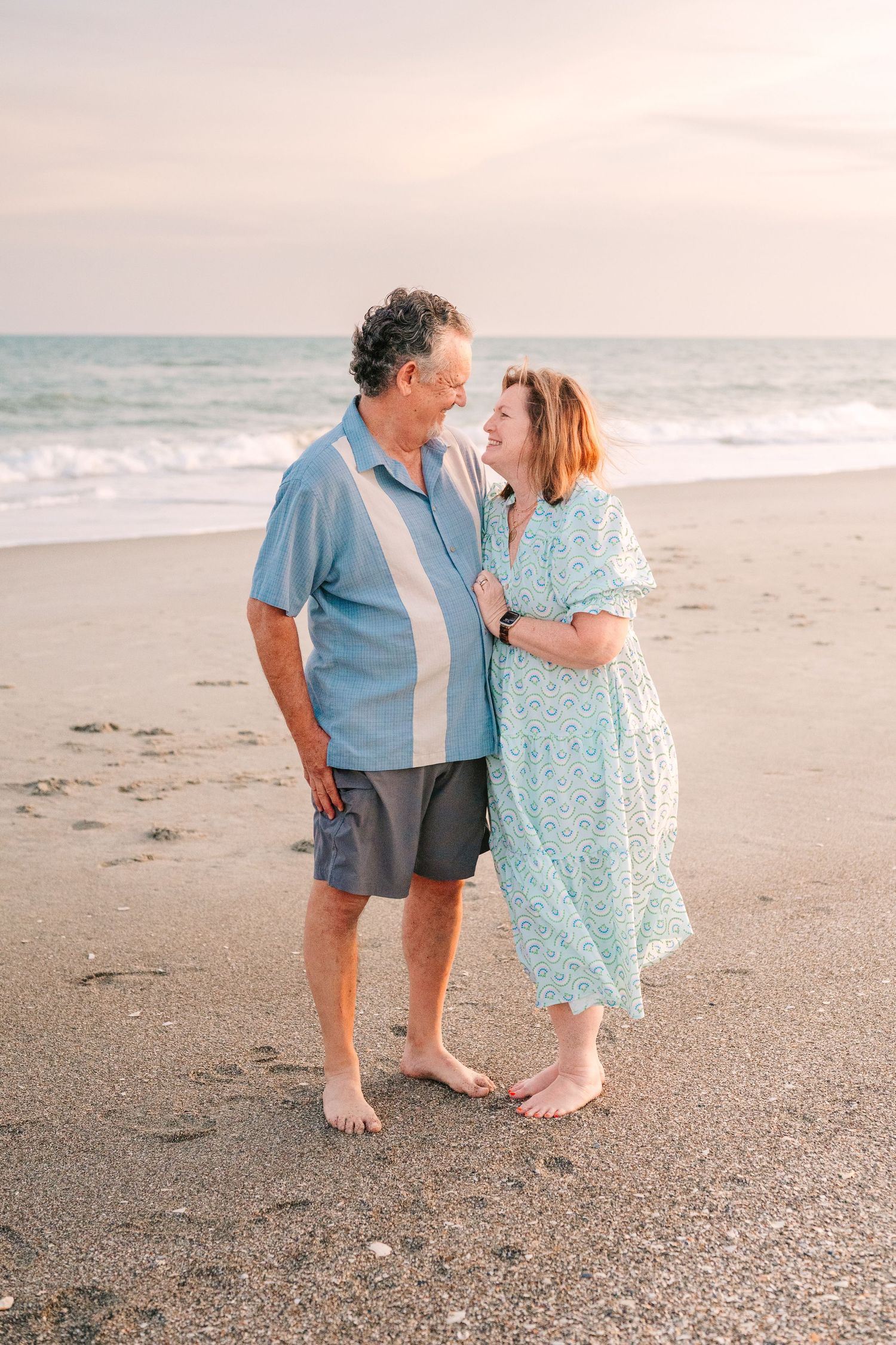 A loving couple shares a tender moment while standing barefoot on a peaceful beach at dusk.