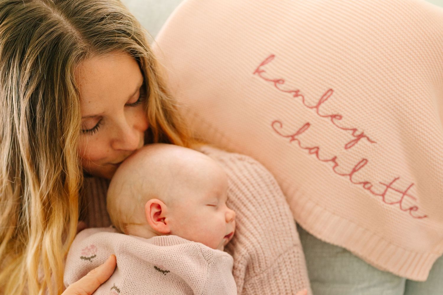 A parent lovingly holds and snuggles with their sleeping baby while wearing cozy knit sweaters.