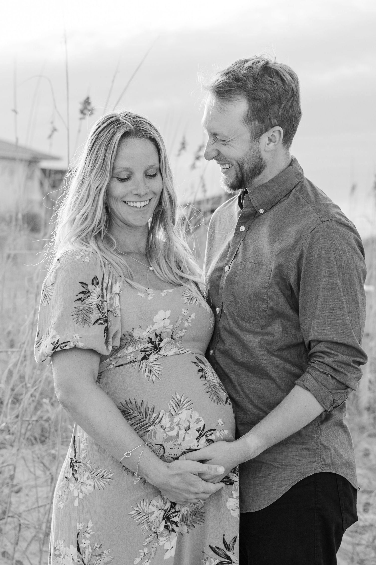 Black and white maternity photo showing a couple embracing outdoors with the expectant mother wearing a floral dress.