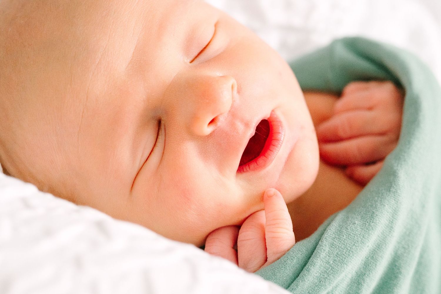 A peaceful sleeping baby wrapped in a soft mint green blanket rests with mouth slightly open.